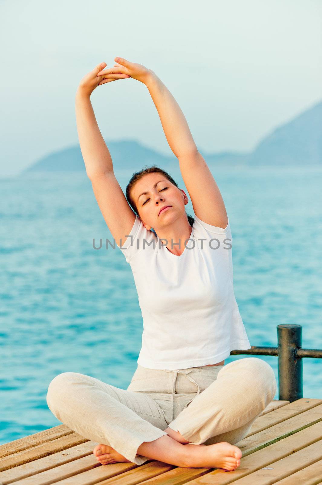 beautiful woman stretching in the morning while sitting on a pier at the sea