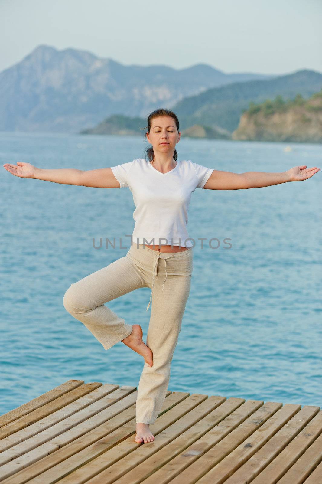 girl by holding a balance while standing on one leg on pier by kosmsos111