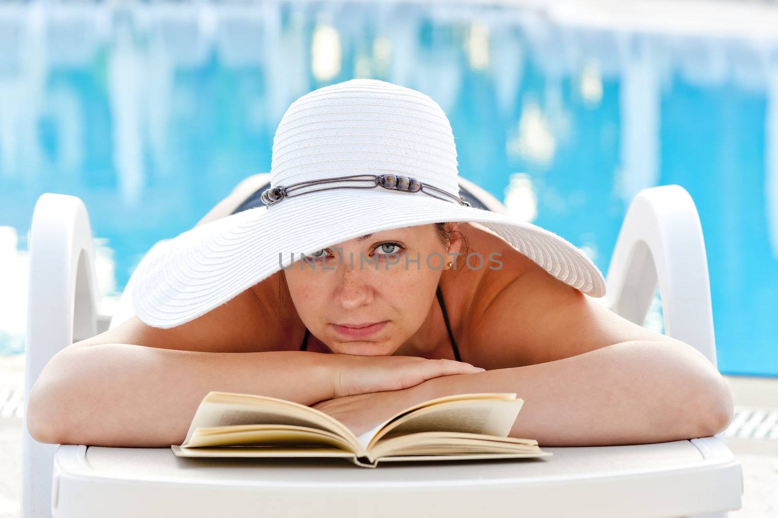 woman lying in a deck chair with a book and sunbathing near the pool