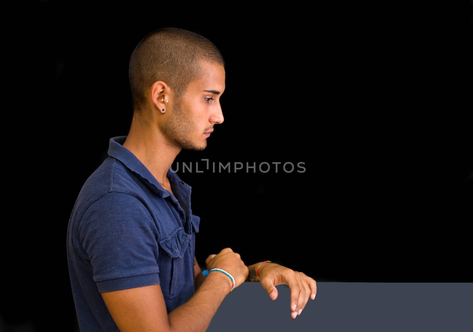 Attractive young man, side view, looking down with hands on grey board, isolated on black