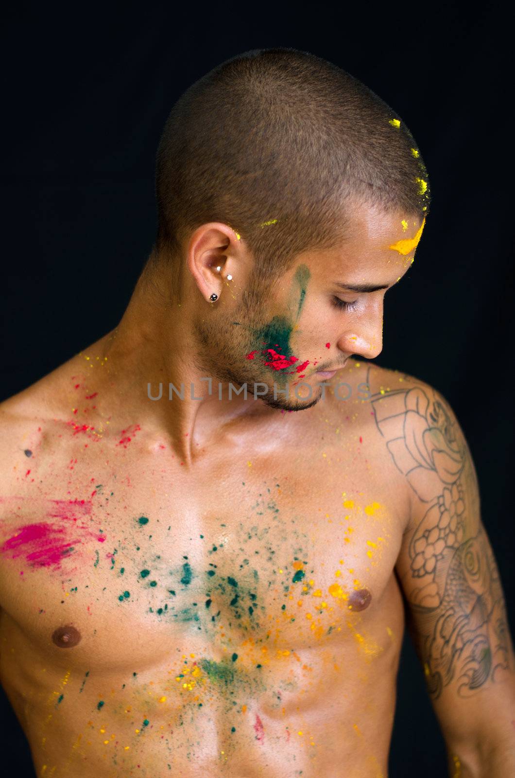 Attractive young man shirtless, skin painted all over with bright Honi colors, looking down