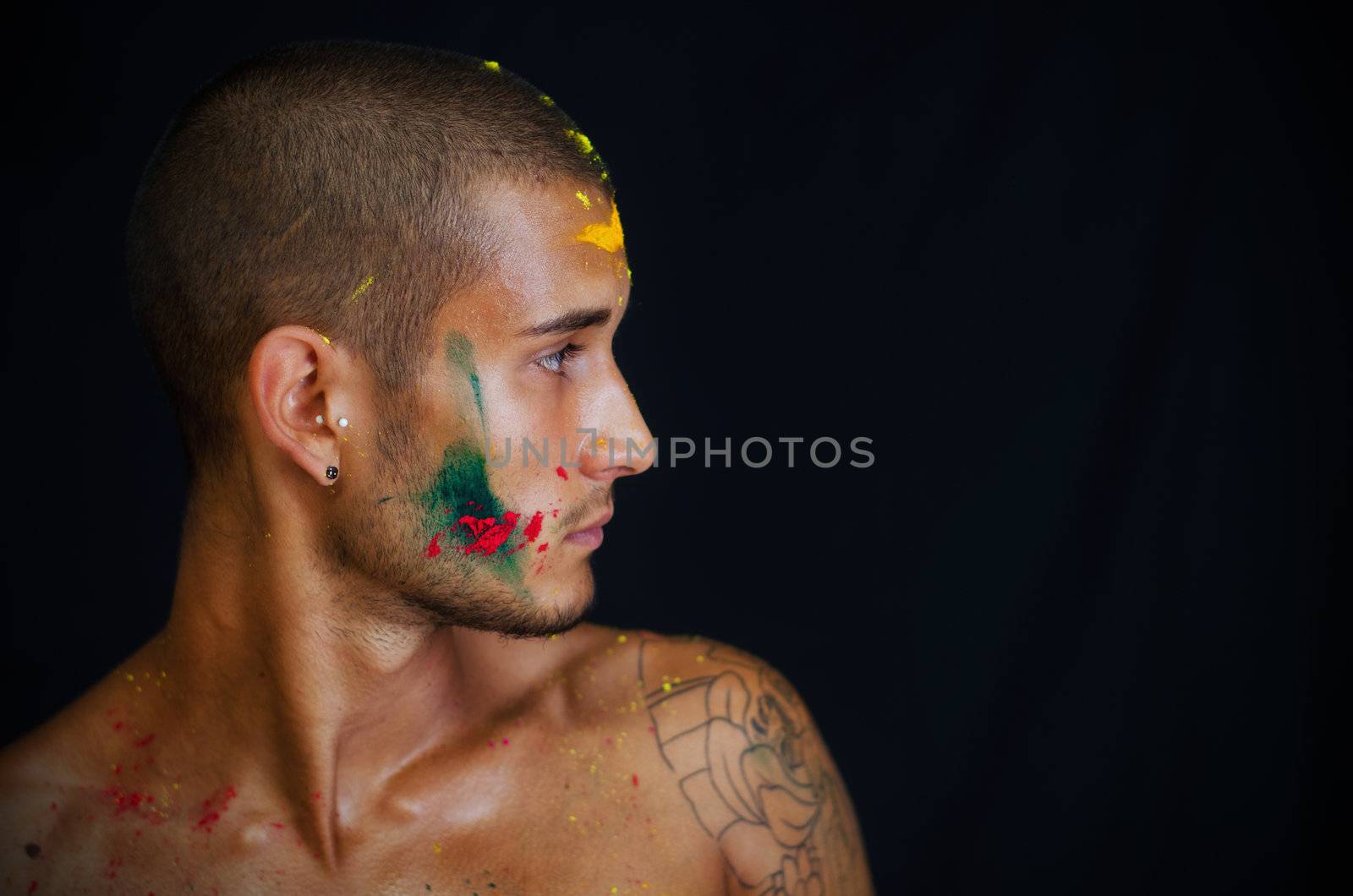 Attractive young man shirtless, skin painted all over with bright colors looking to a side, profile view