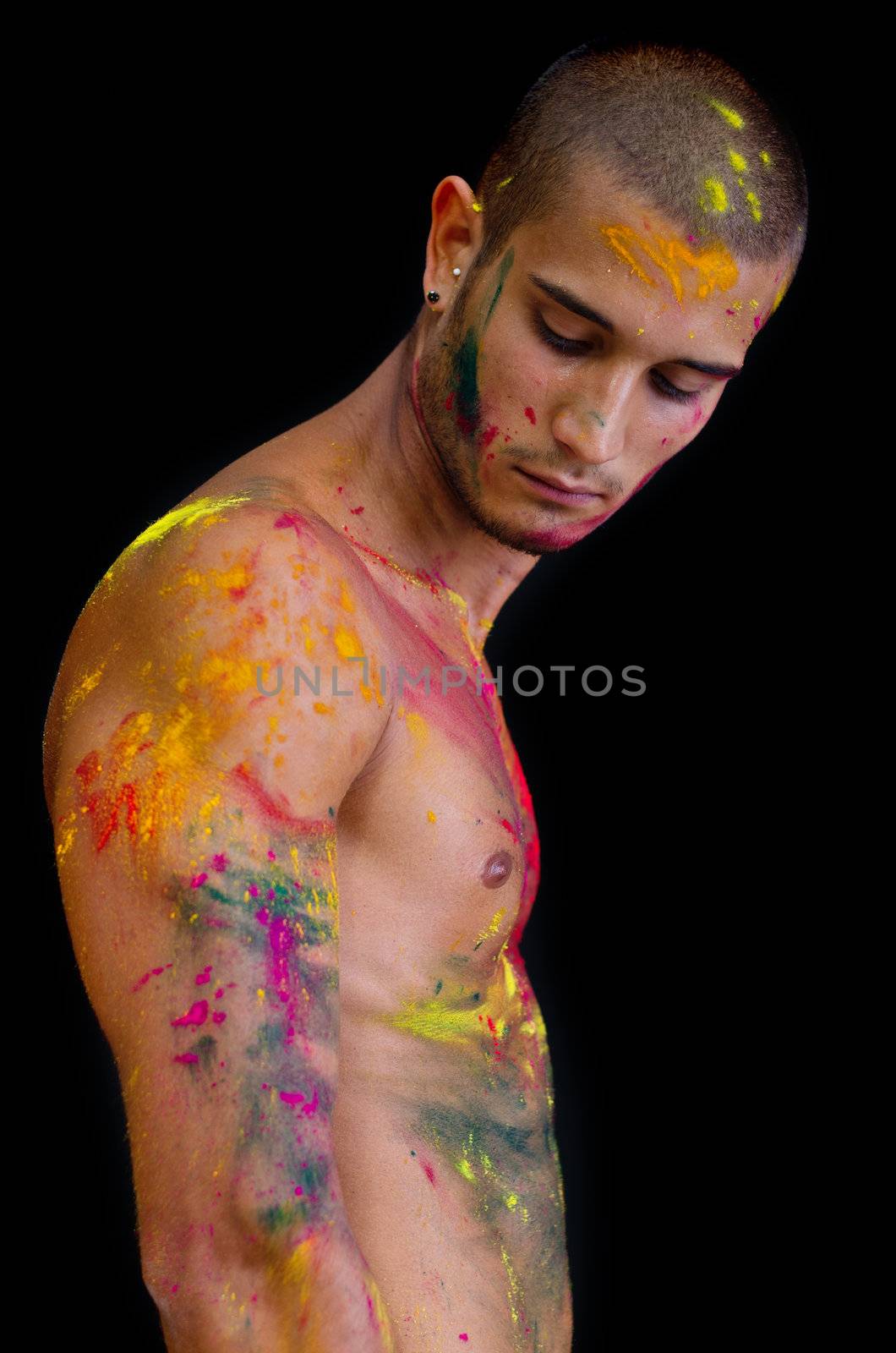 Handsome young man with skin all painted with colors looking down, isolated on black background