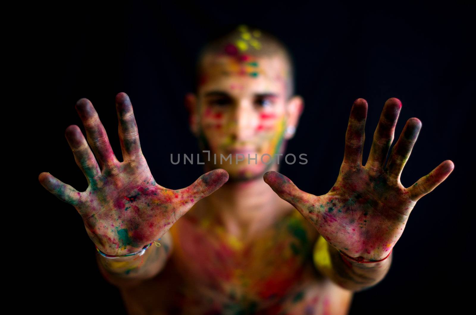 Attractive young man showing all colored hands in foreground. All skin is painted with colors