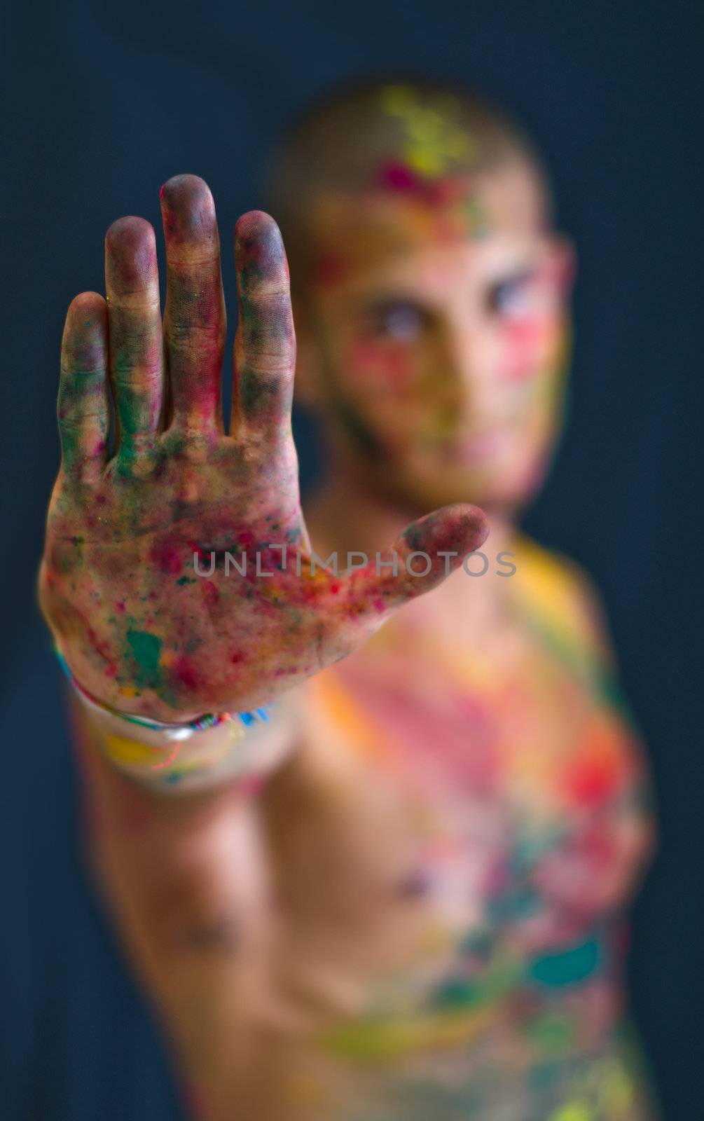 Attractive young man showing all colored hand in foreground. All skin is painted with colors