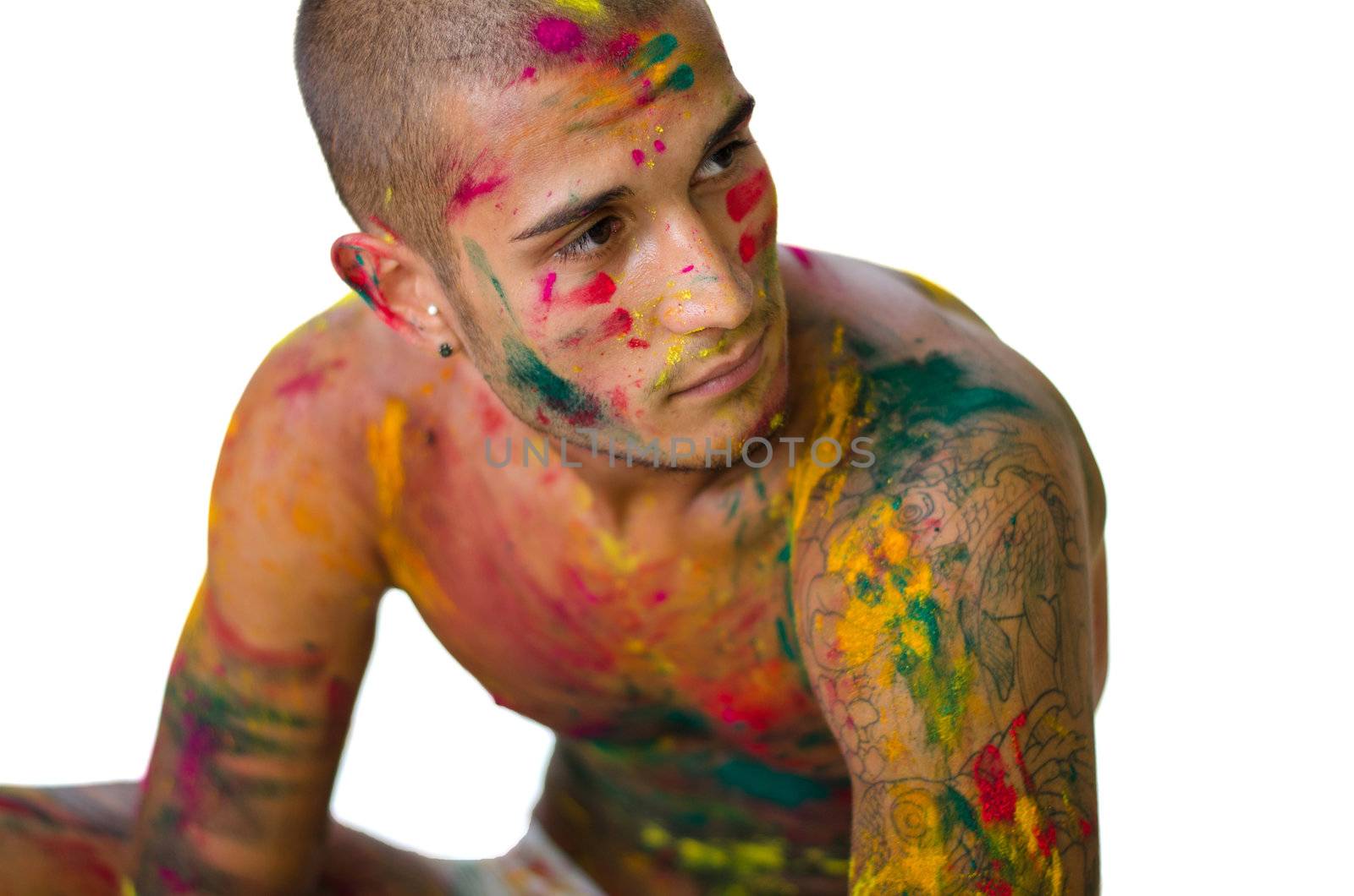 Handsome young man with skin all painted with colors sitting on the floor, isolated on white