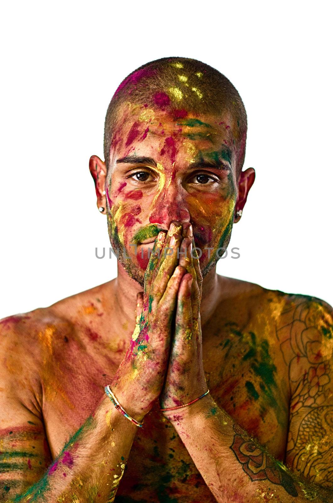 Attractive young man shirtless, skin painted all over with bright colors and hands in front of his mouth, grinning