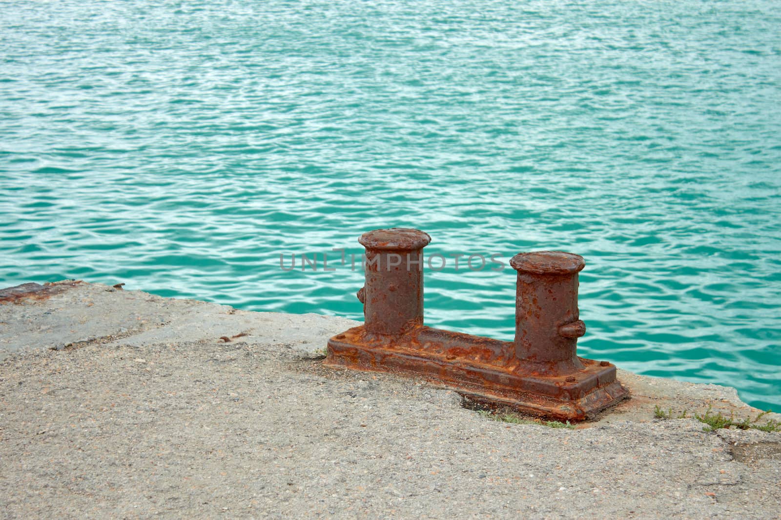 Steel rusty dual mooring bitt on a fragment of old concrete pier on the background turquoise sea water