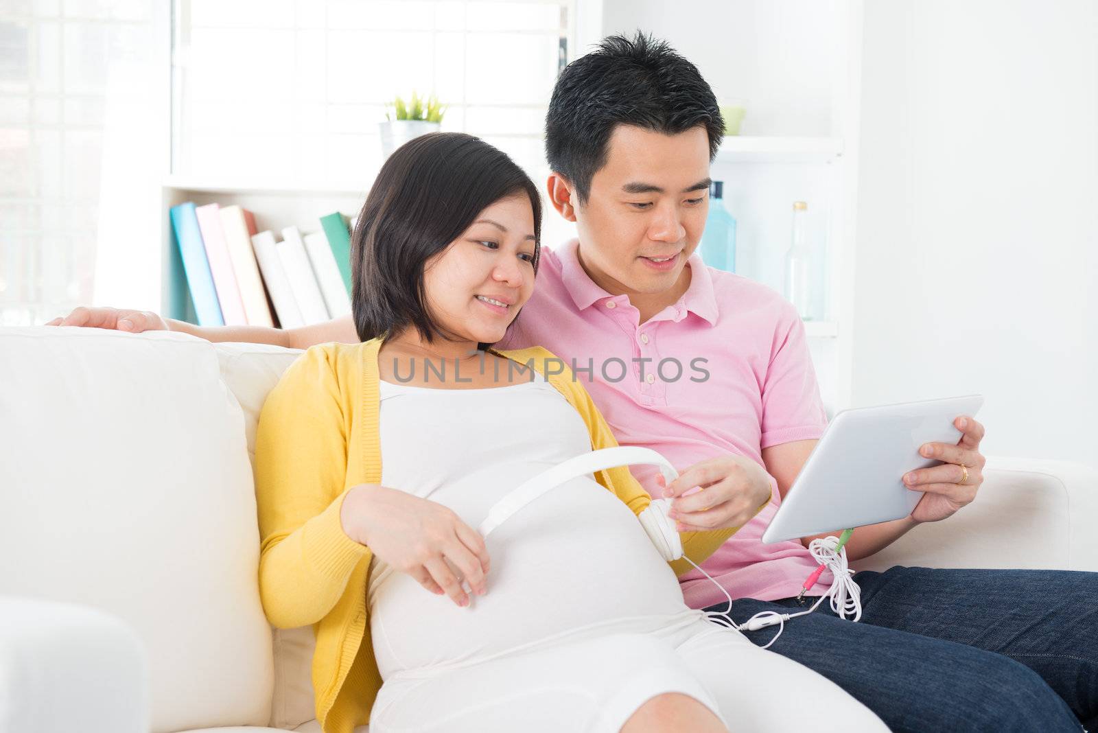 Pregnant woman putting headphones on her belly. Asian pregnant couple living lifestyle.