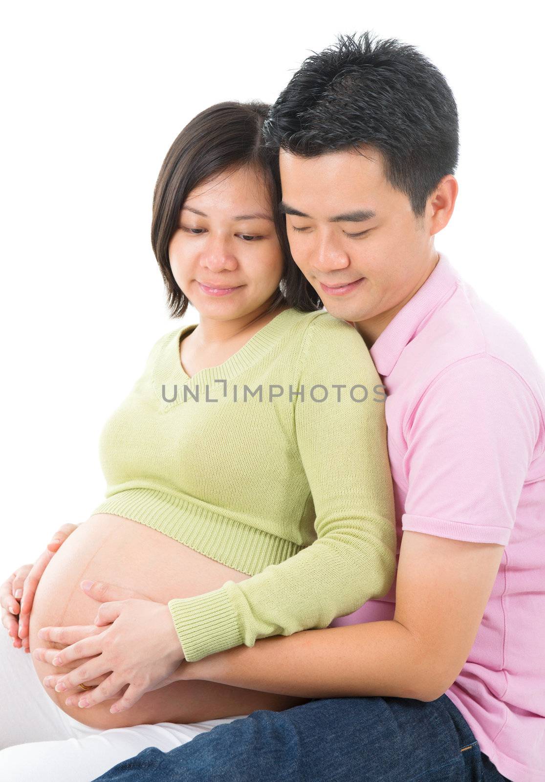 Affectionate Asian pregnant couple sitting isolated on white background.