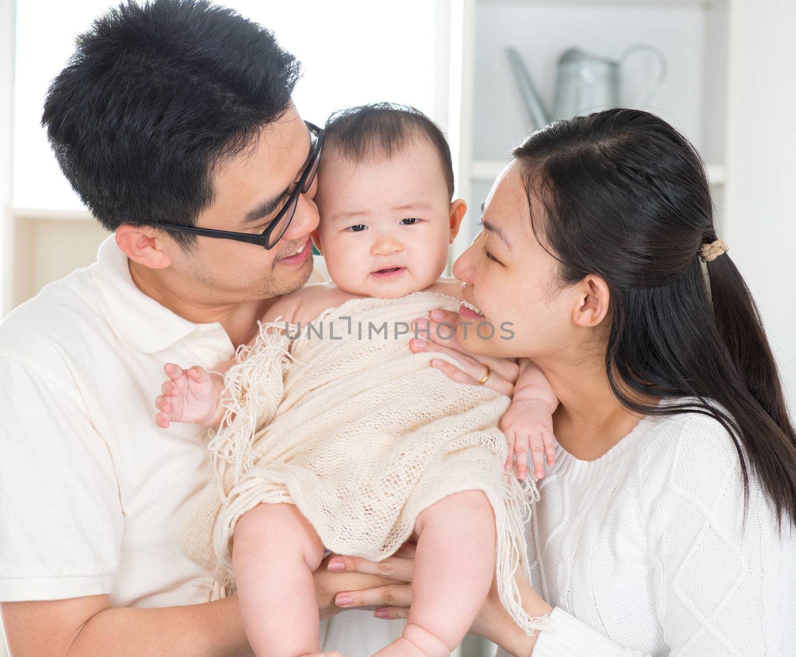 Asian parents kissing six months old baby girl at home.