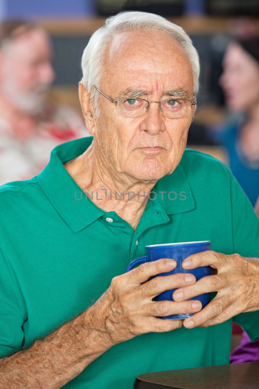 Sulky senior male holding coffee mug in cafe