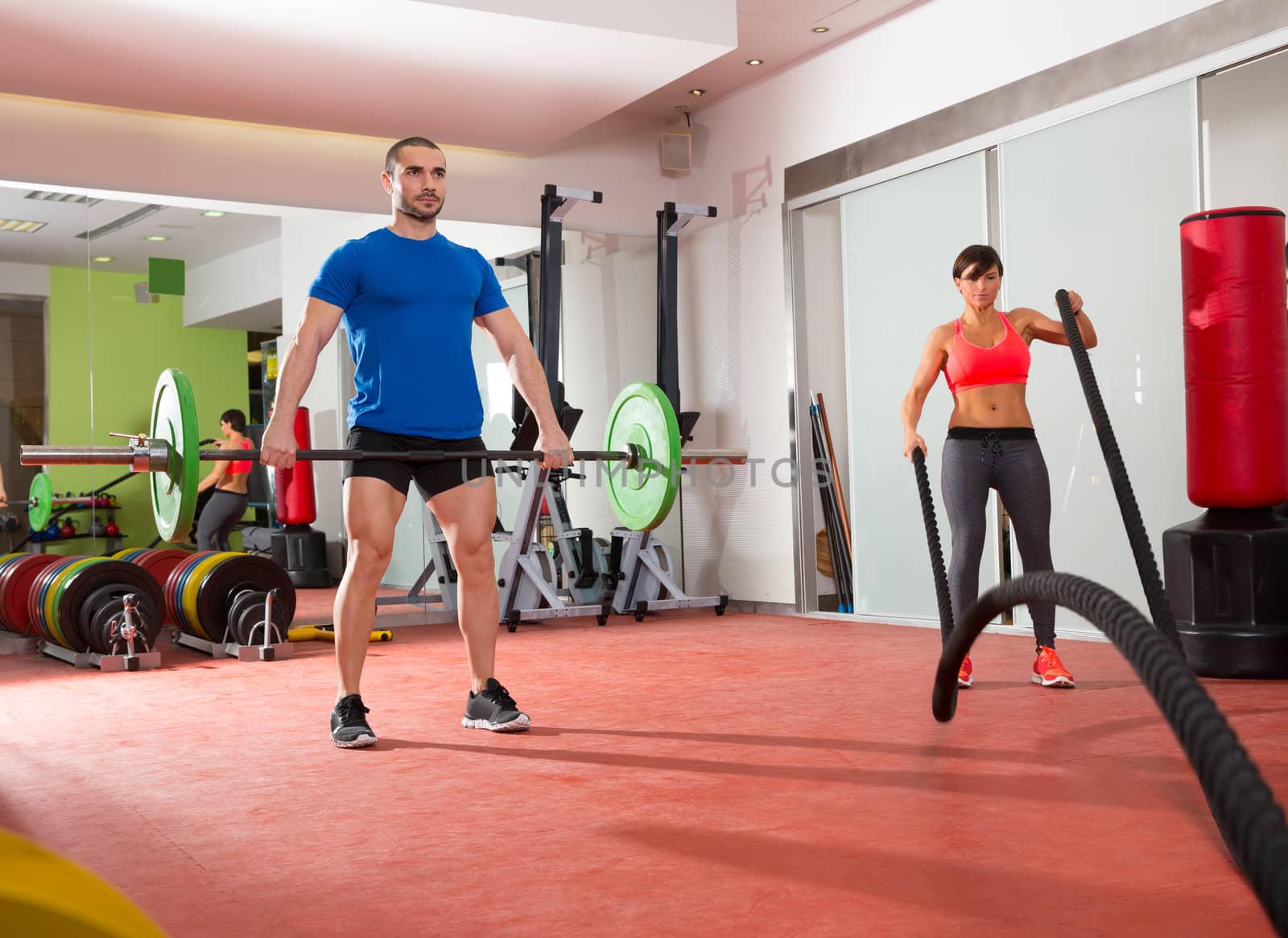 Crossfit gym weight lifting bar man woman battling ropes by lunamarina