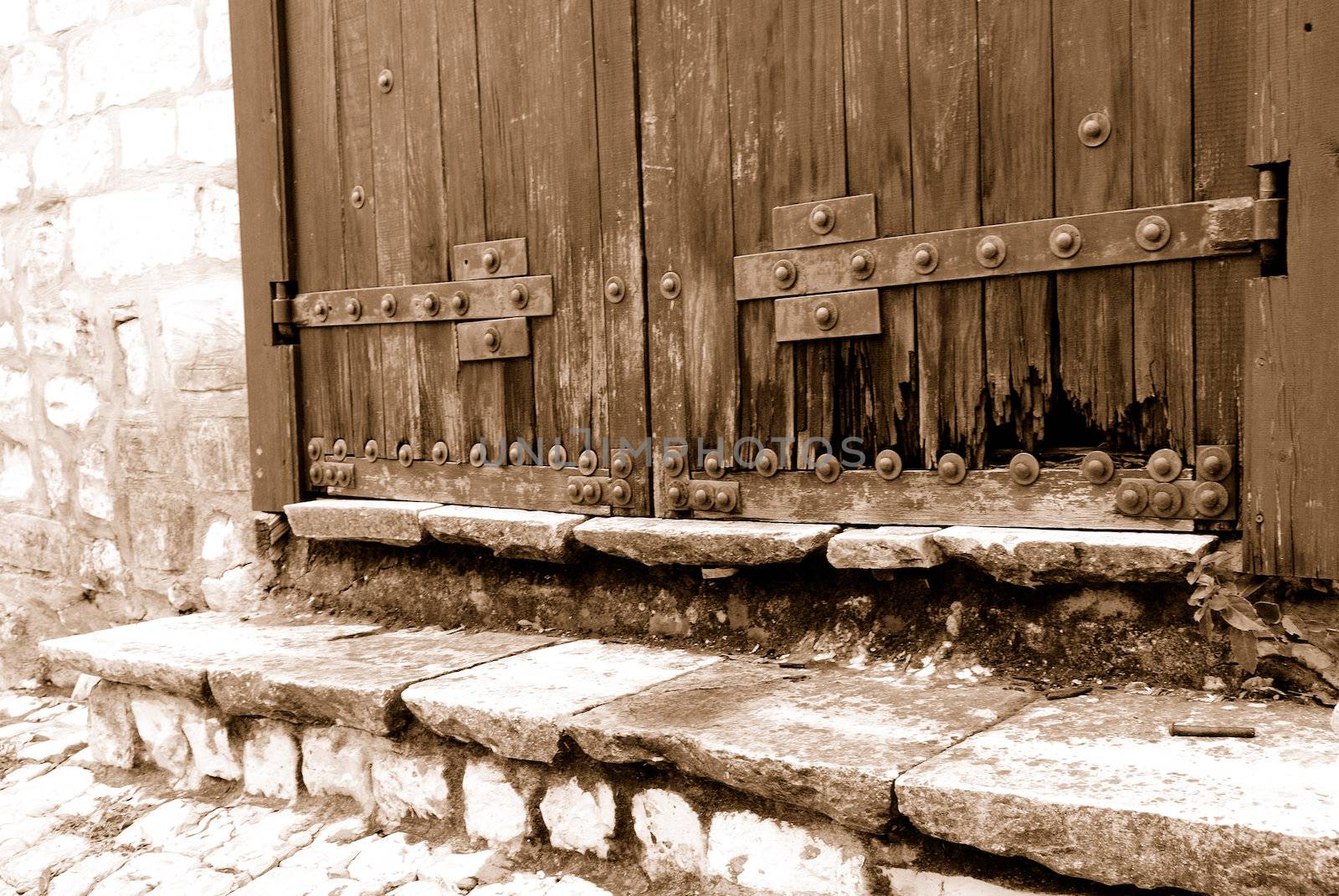 Lower part of an old heavy wooden door in ancient house. Sepia 