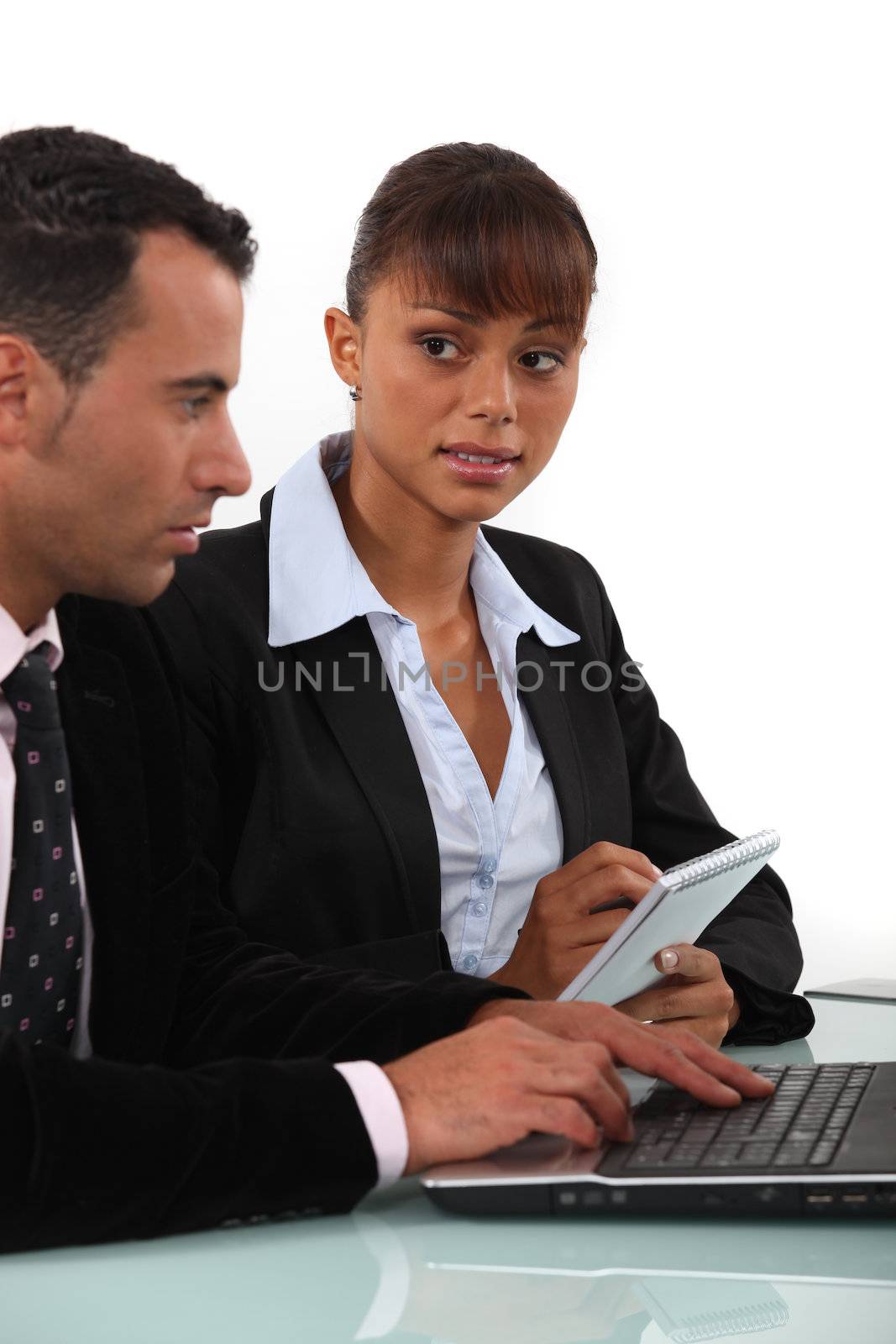 Woman taking notes as a businessman uses a computer by phovoir