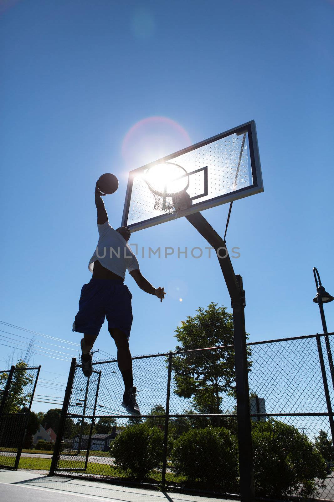 A young basketball player going up for a dunk.  Intentionally back lit with bright lens flare coming through the clear backboard.