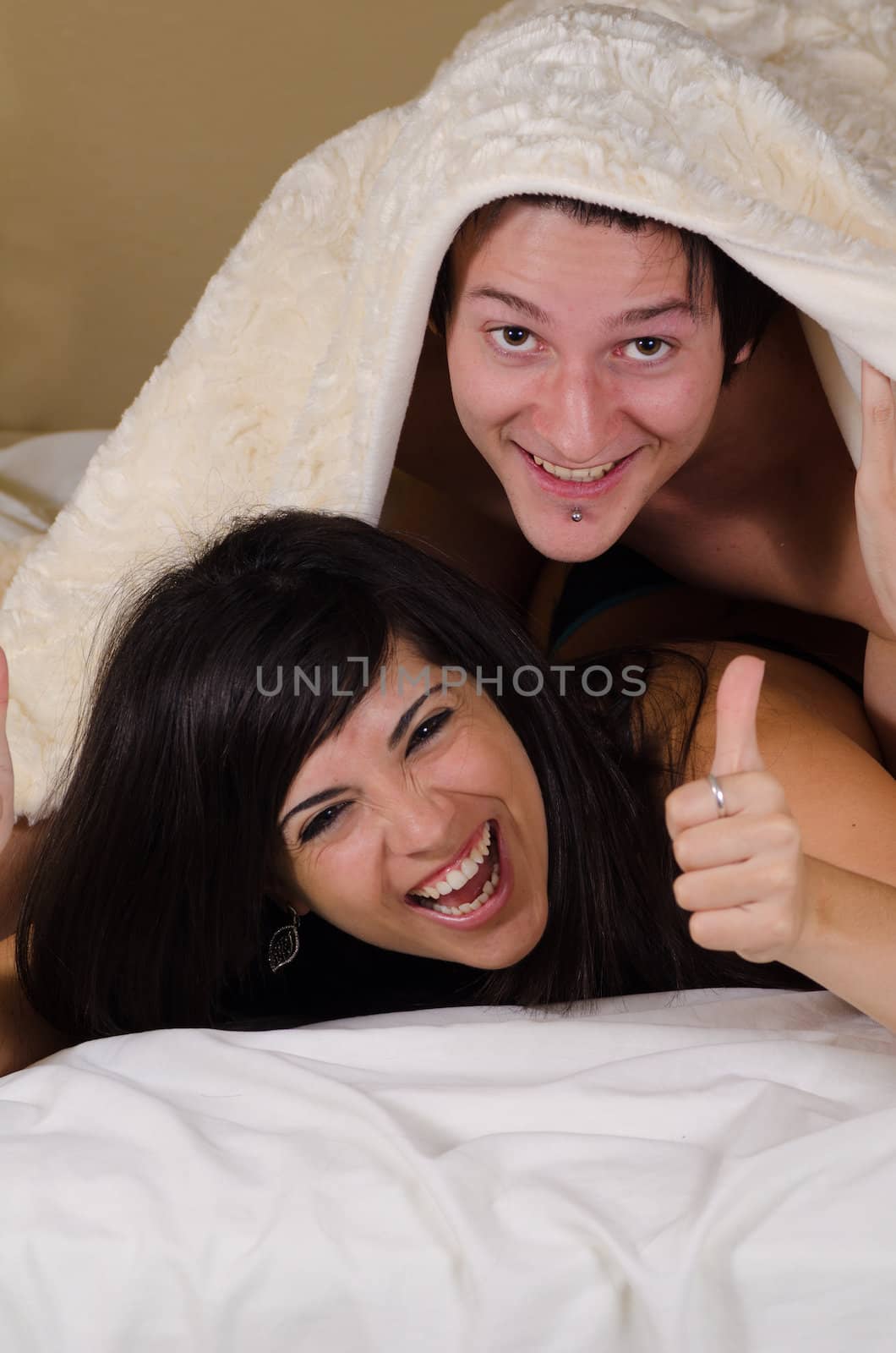 Happy couple smiling at camera from under a blanket