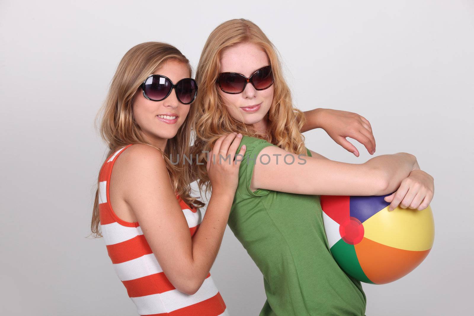 Two teenagers wearing sunglasses holding beach ball