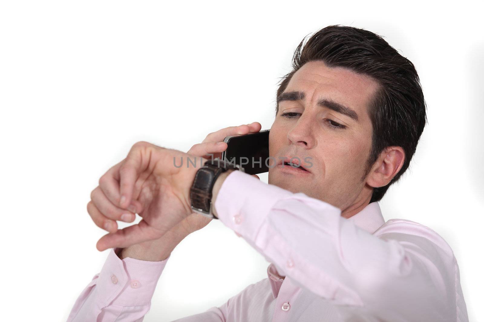 businessman talking on his cell and looking at his watch by phovoir