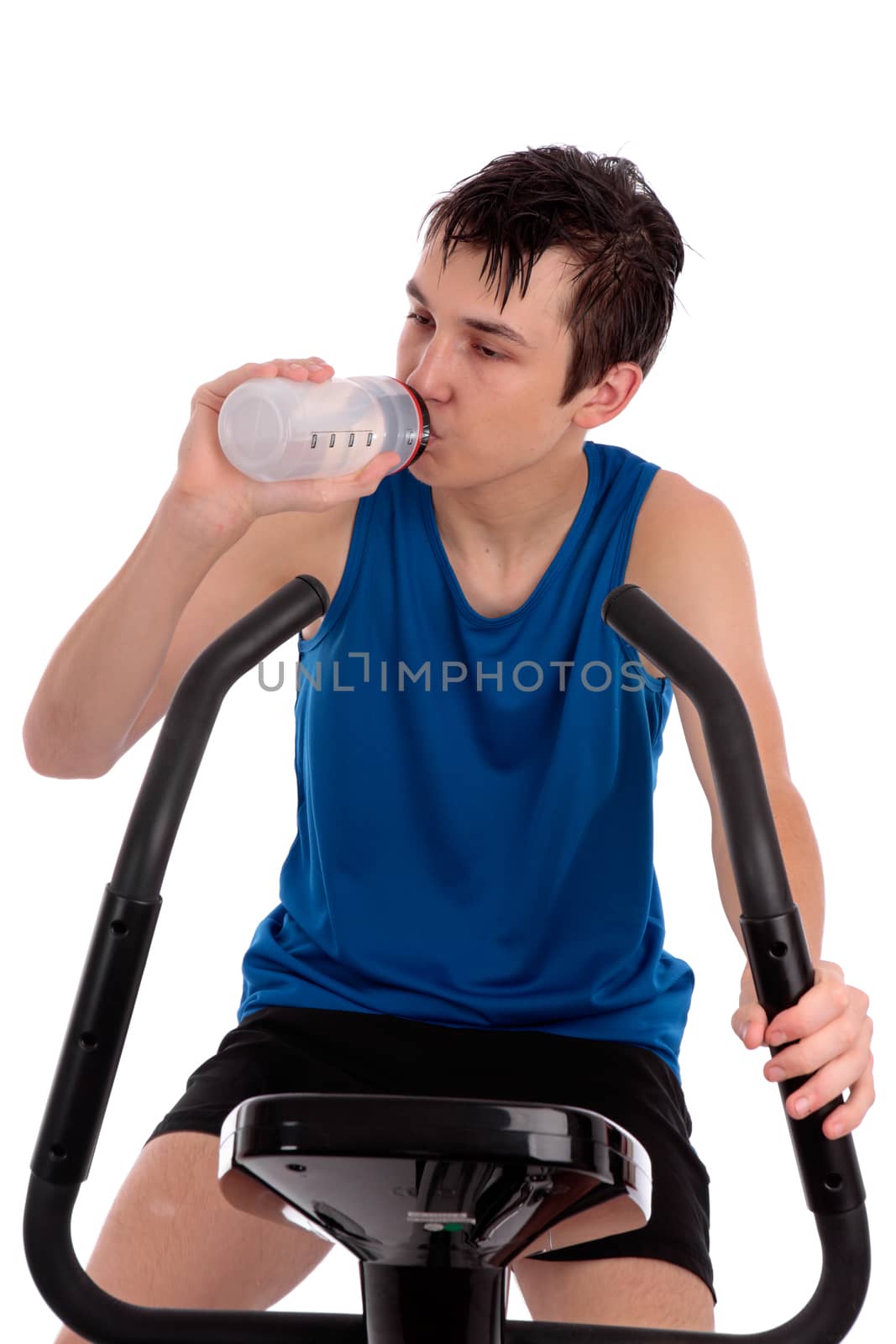 A teenage boy using an exercise bike for fitness.  He is drinking water.  White background.