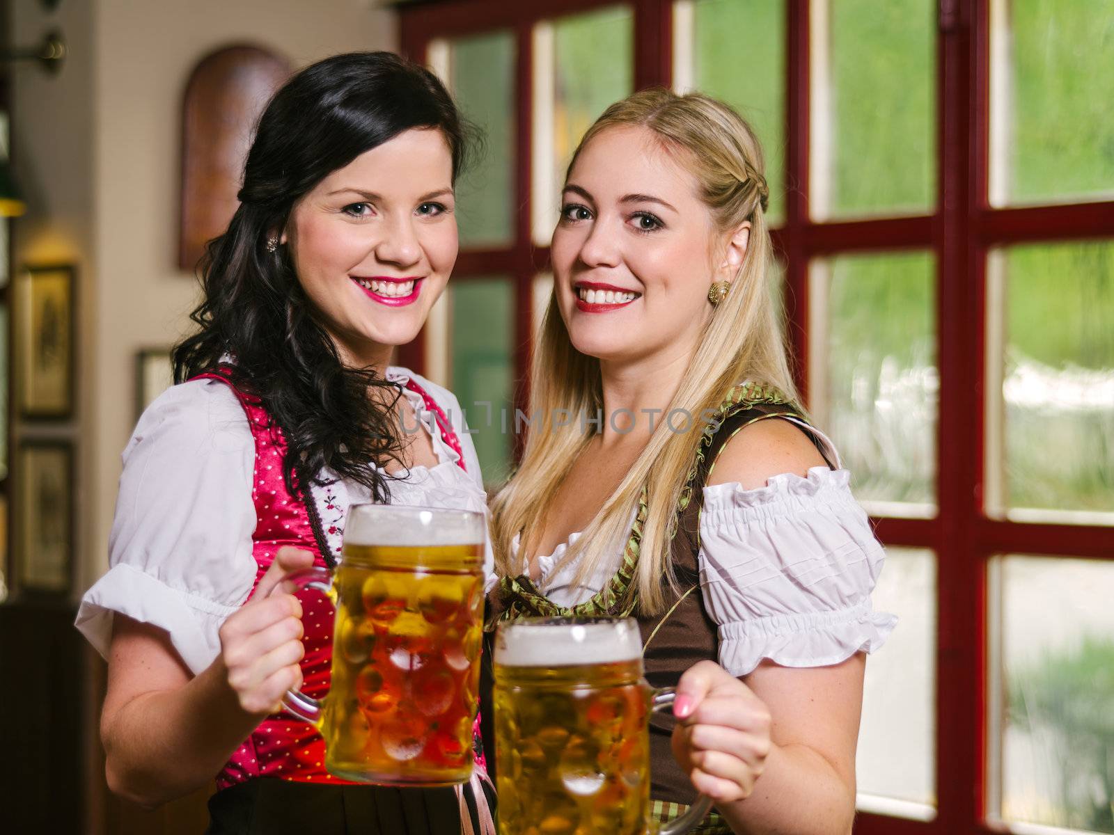 Photo of two beautiful female waitresses wearing traditional dirndl and holding huge beers in a pub.