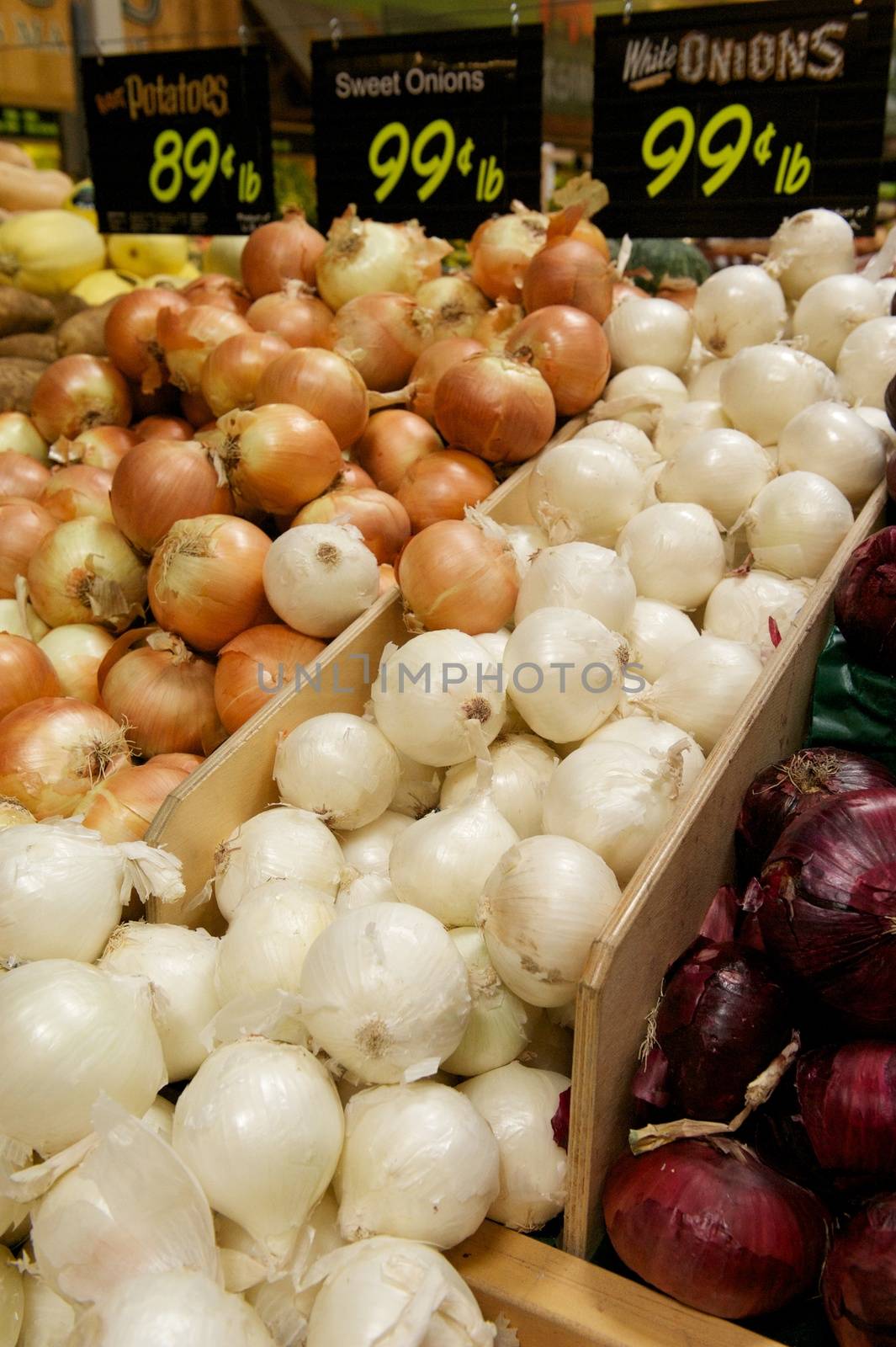 Wooden grocery store bins full of White, Yellow and Red Onions with signs listing their prices
