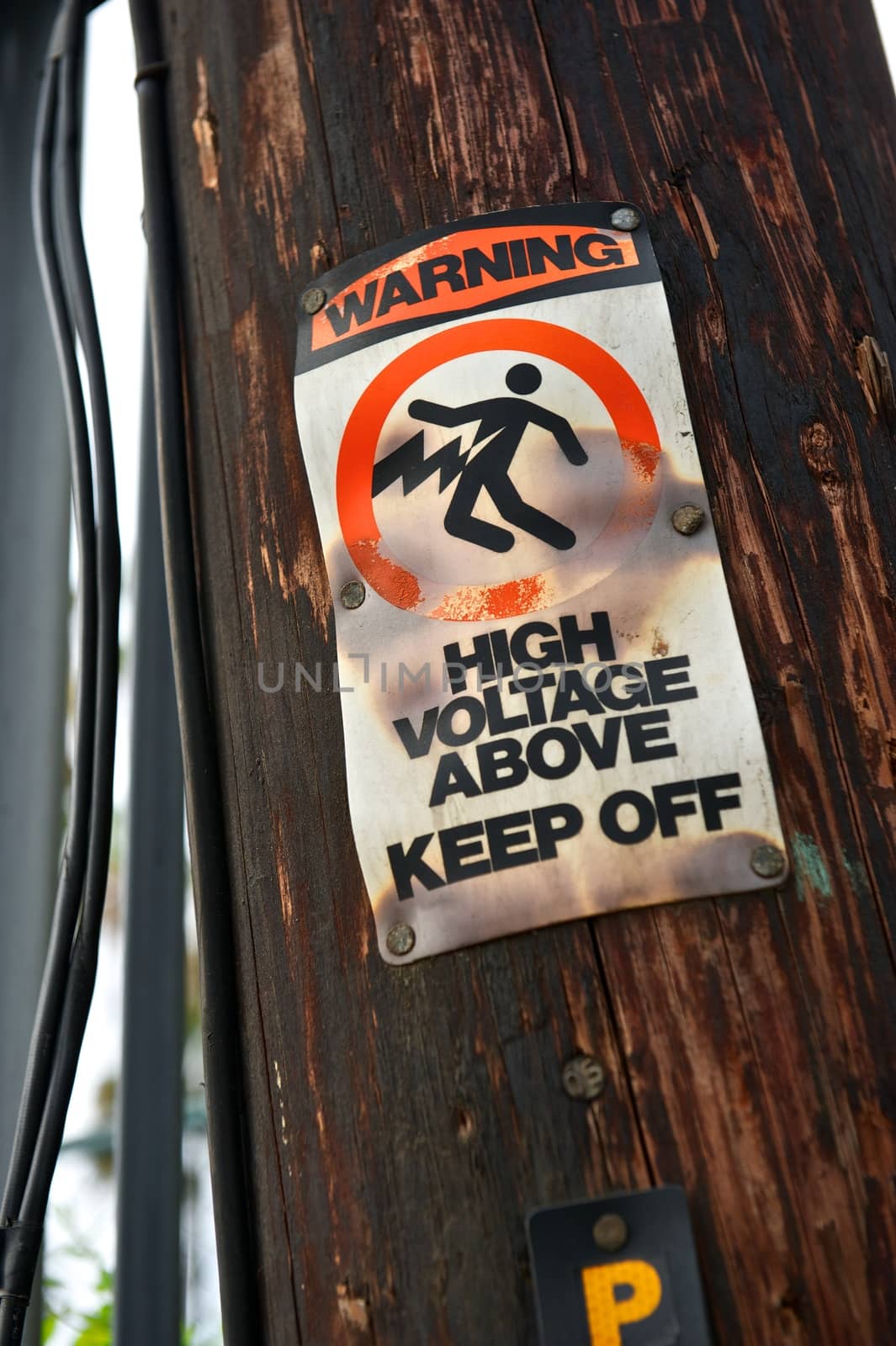 Damaged and blackened warning sign with High Voltage Above and Keep Off posted on an old telephone pole