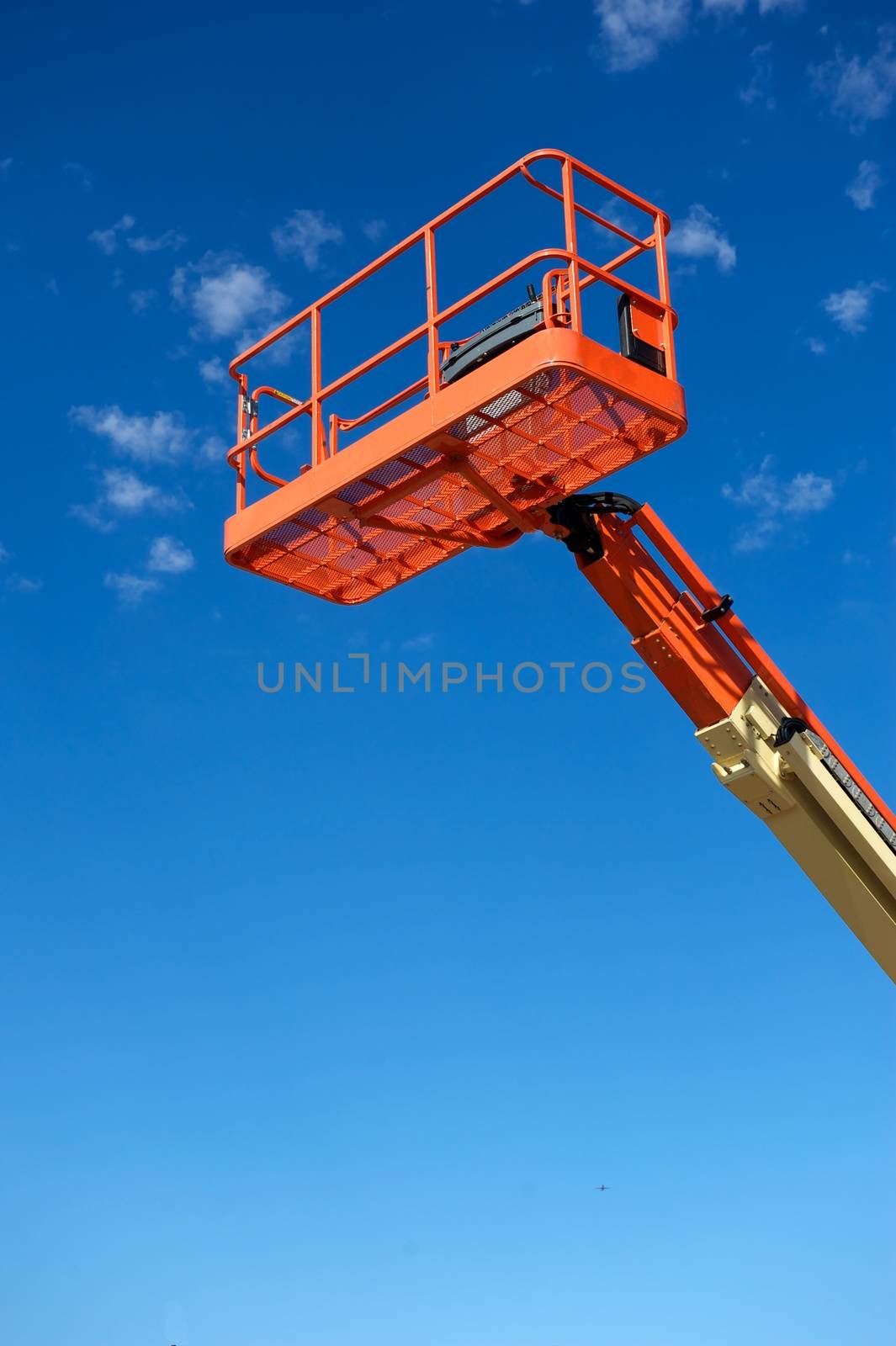 Orange hydraulic utility lift used in the construction industry shot against a blue sky with white clouds