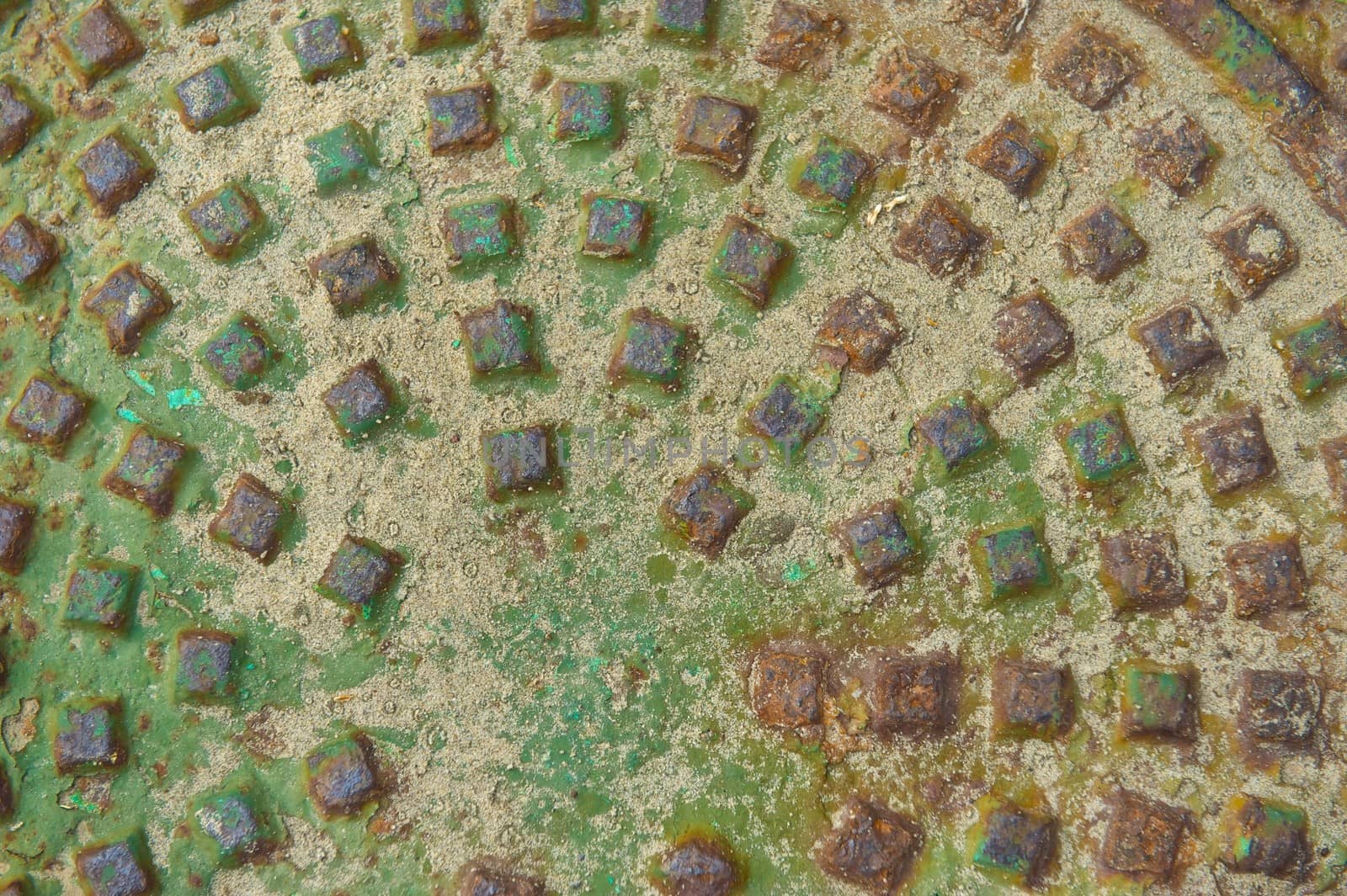 Oxidized man hole cover with rust stains and sand that includes a pattern of raised squares