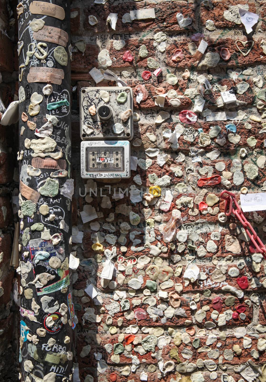 Verona, Italy – July 18, 2013: Colorful bubble gums with remnants of love notes stuck to the ancient brick wall and adjoining gutter in the courtyard of Juliet's House tourist attraction in Verona, Italy.