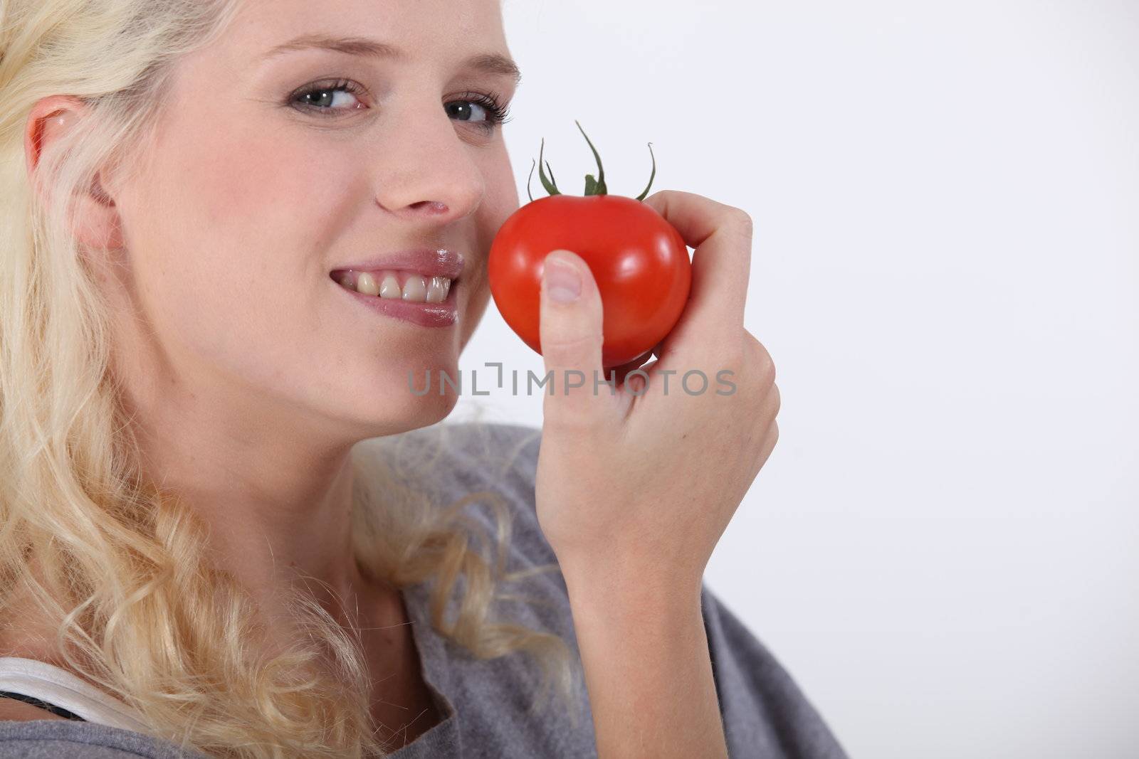 Young woman eating a tomato by phovoir