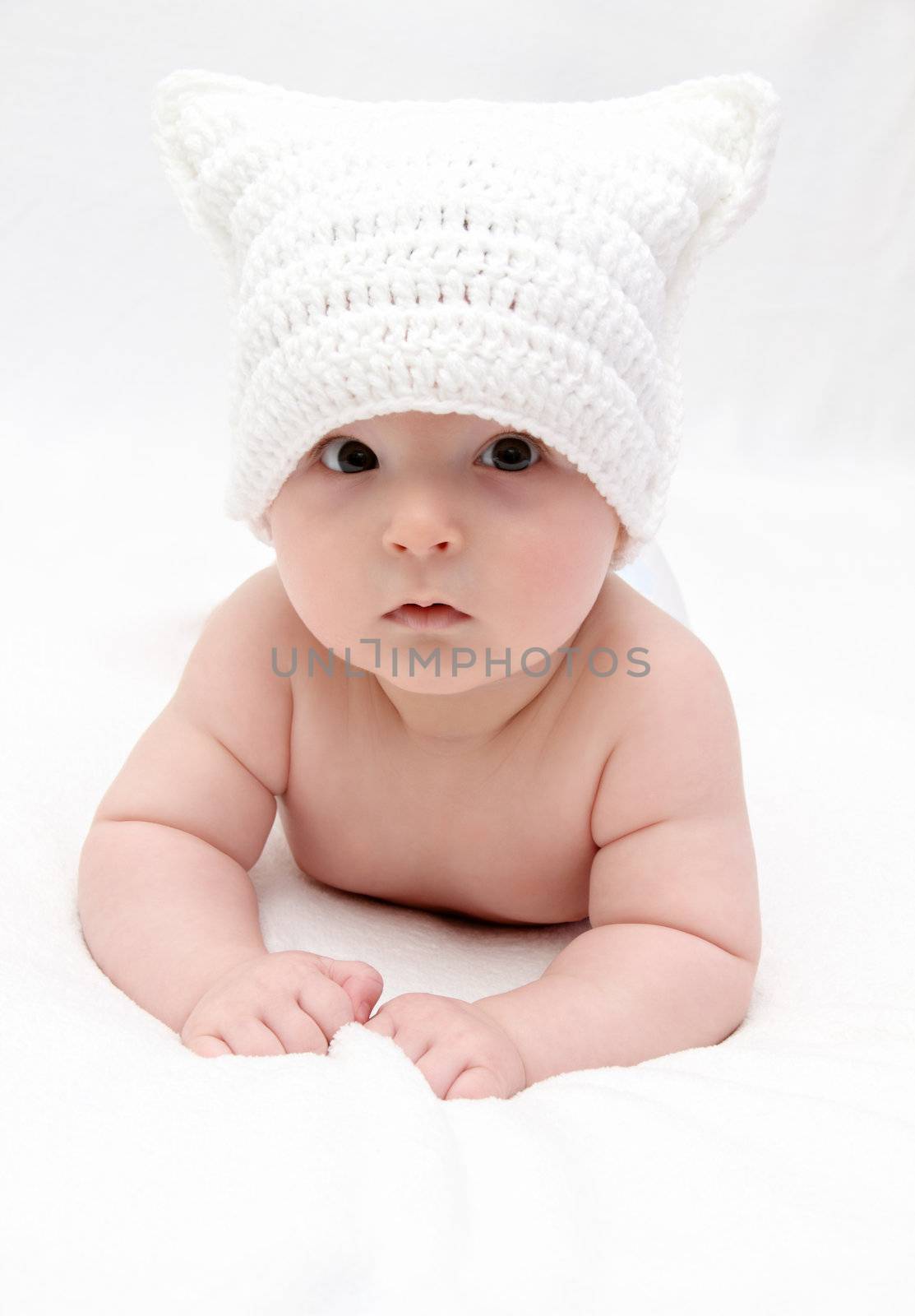 Beautiful baby in white hat lies on bed