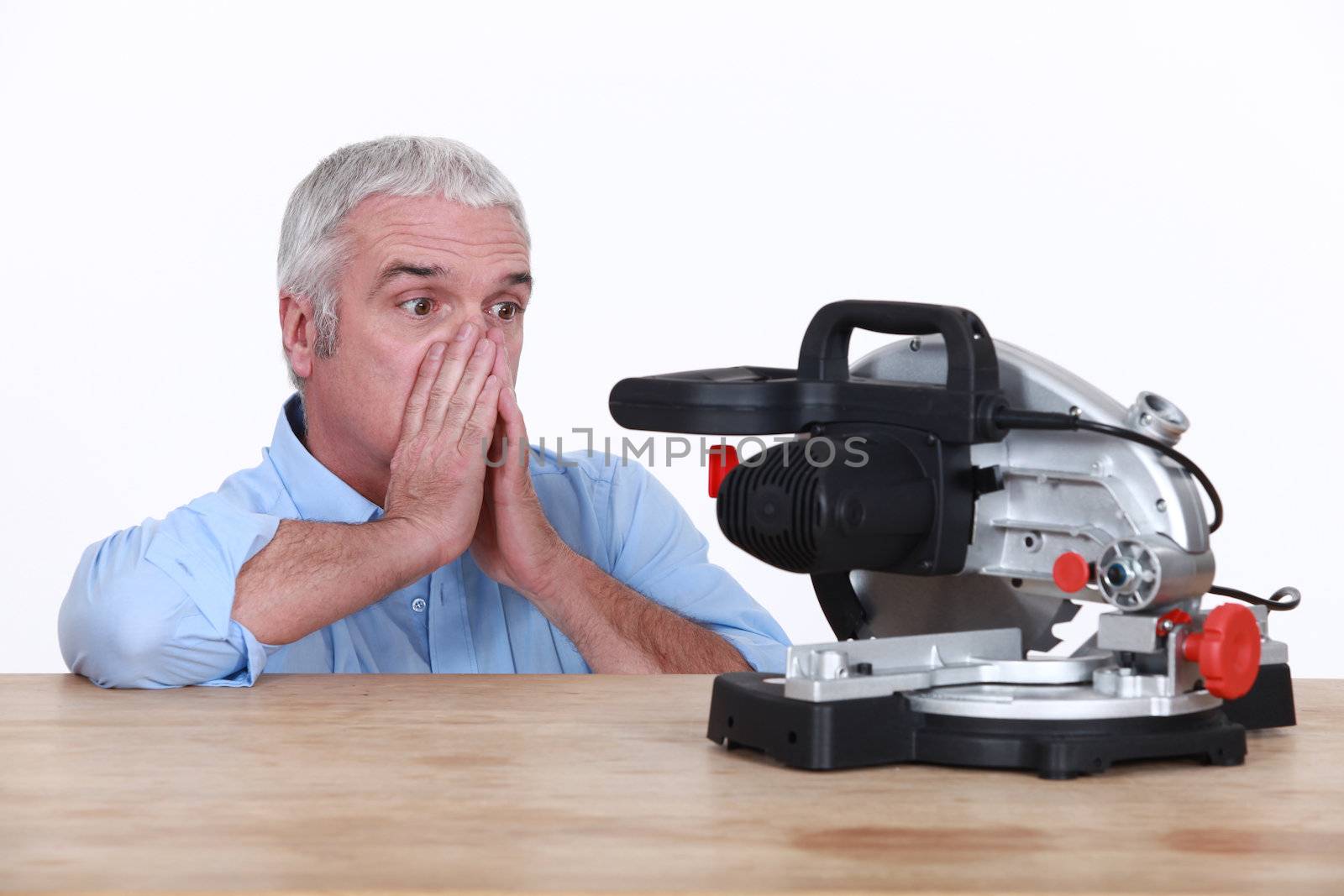 Mature looking at his circular saw with disarray by phovoir