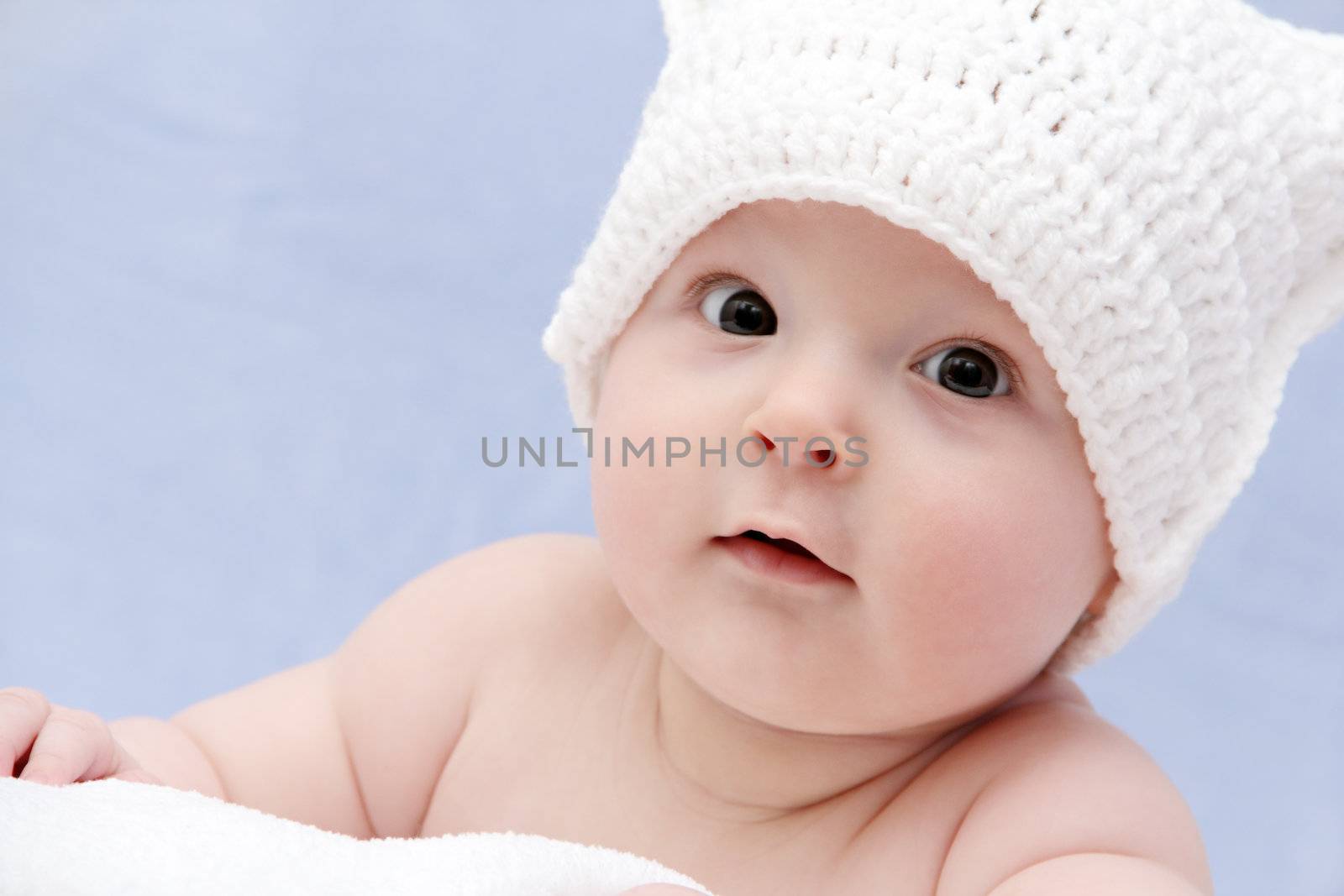 baby in white hat lies on bed by NikolayK