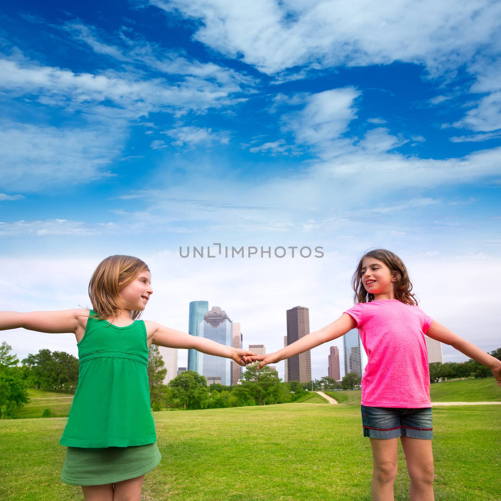 Two sister girls friends playing holding hand in urban modern skyline on park lawn