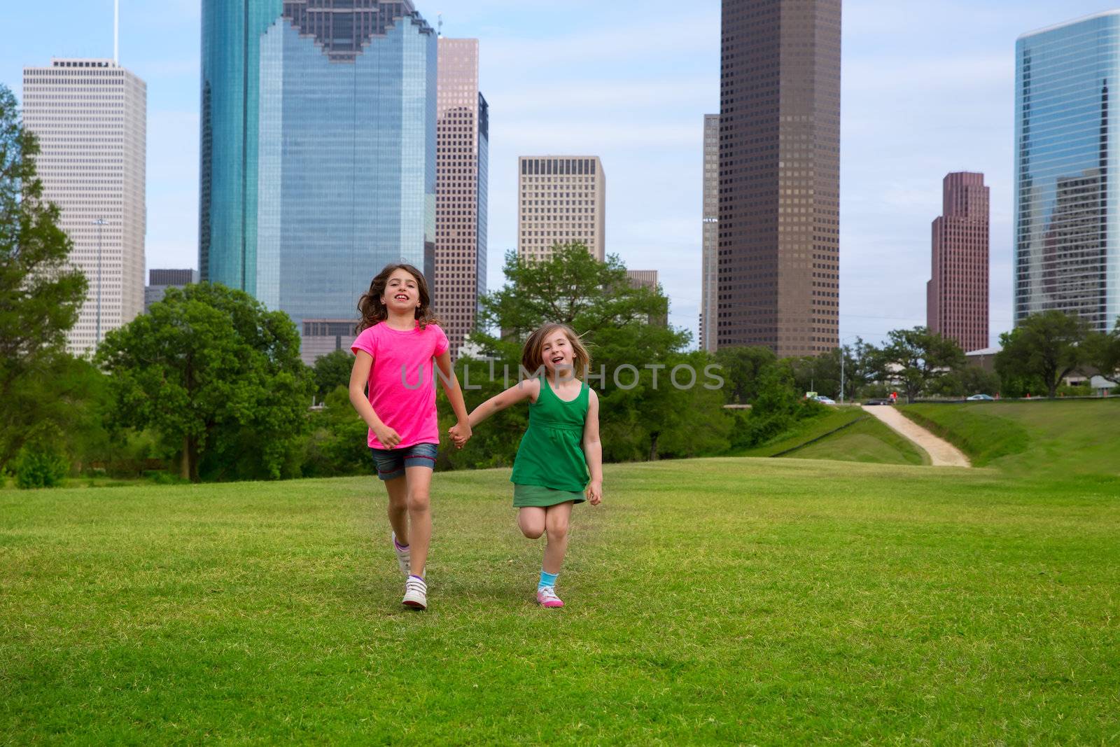 Two sister girls friends running holding hand in urban modern skyline on grass lawn