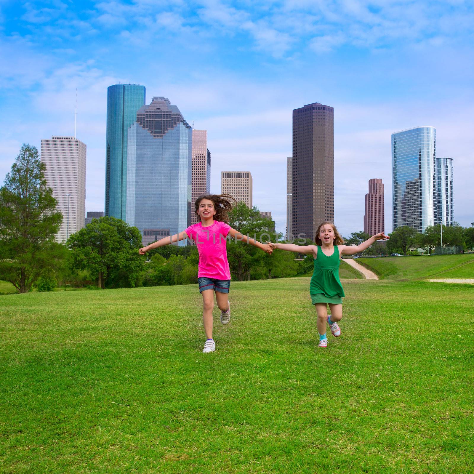 Two sister girls friends running holding hand in urban modern skyline on grass lawn