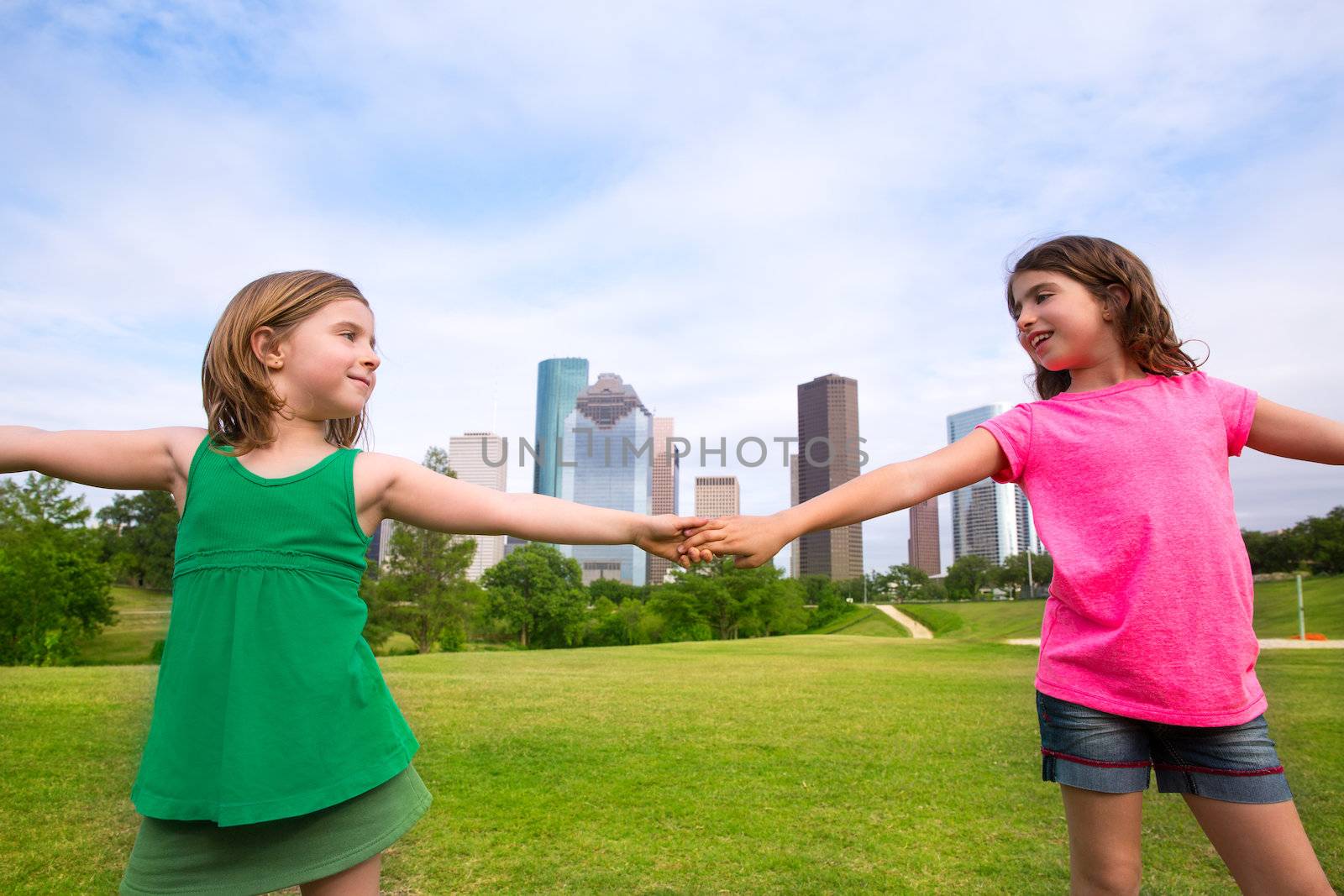 Two sister girls friends playing holding hand in urban modern skyline on park lawn