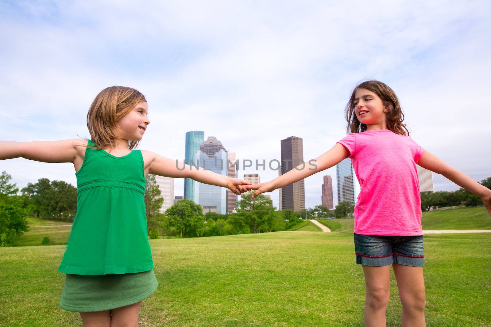 Two sister girls friends playing holding hand in urban modern skyline on park lawn