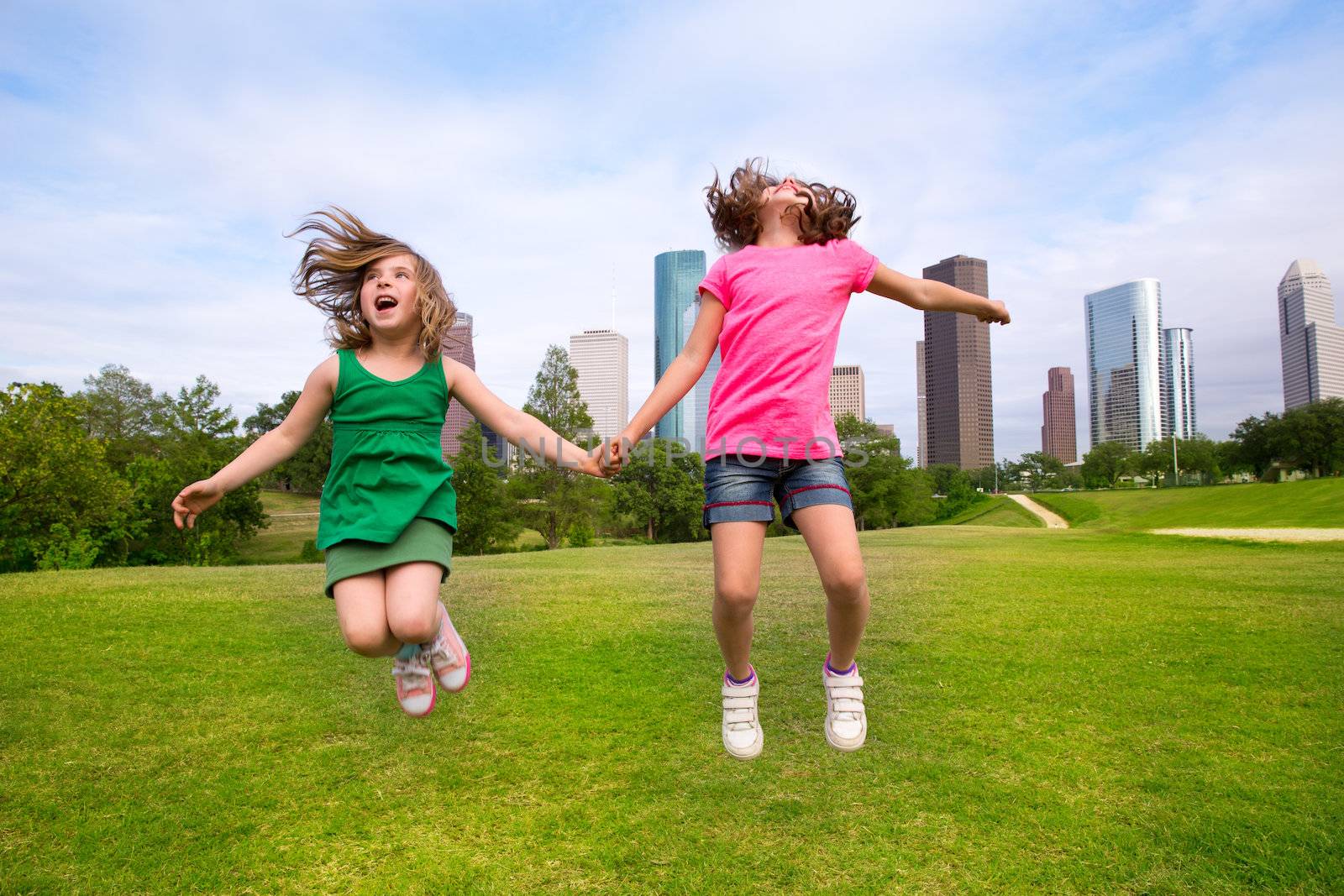 Two girls friends jumping happy holding hand in city skyline by lunamarina