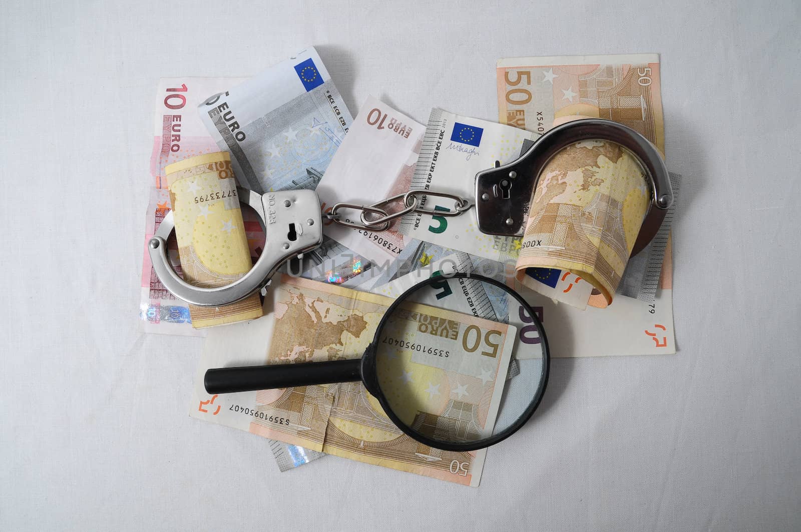 Financial Concept Loupe, Handcuffs and Money on a White Background