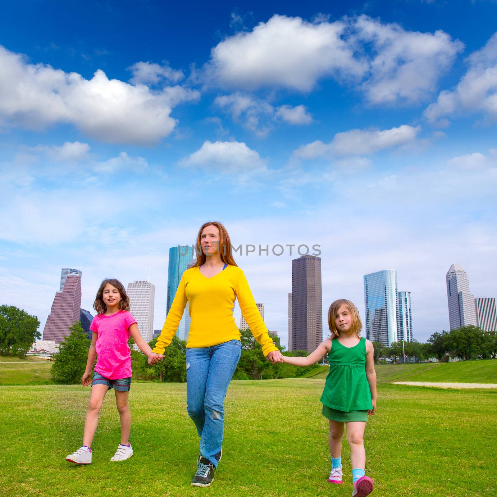 Mother and daughters walking holding hands on city skyline by lunamarina