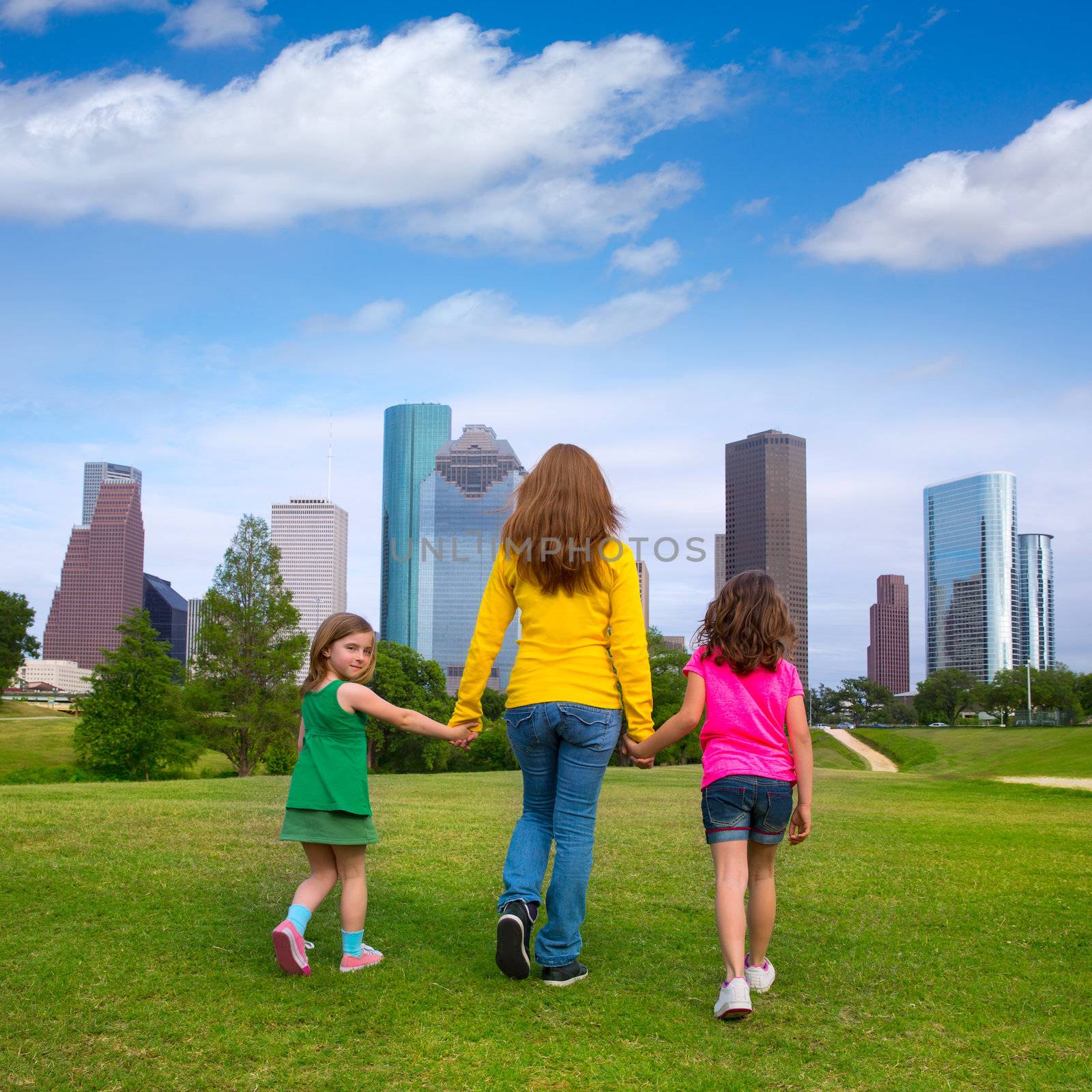 Mother and daughters walking holding hands on modern city skyline over park green lawn