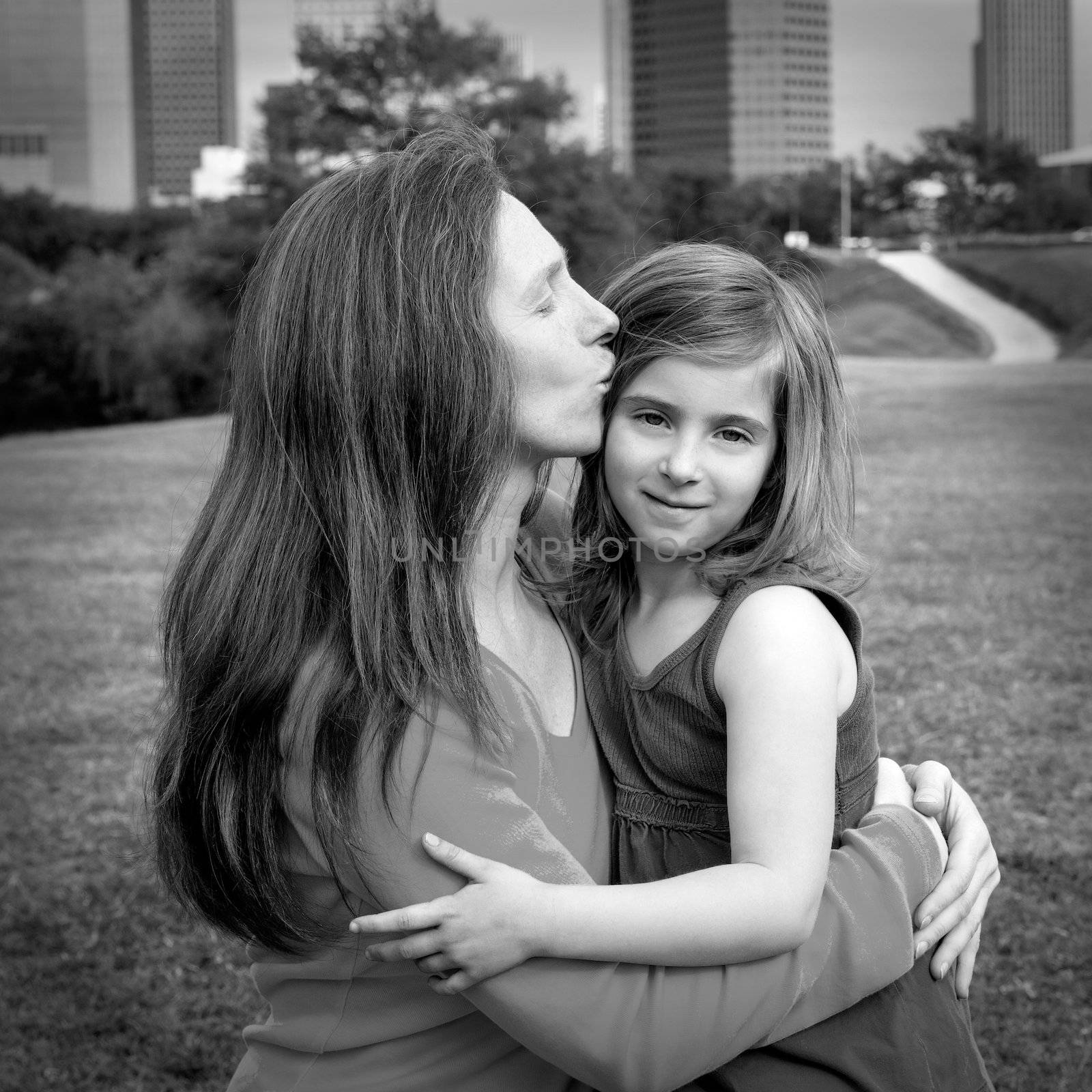 Mother and daughter happy hug kissing in park at city modern skyline background
