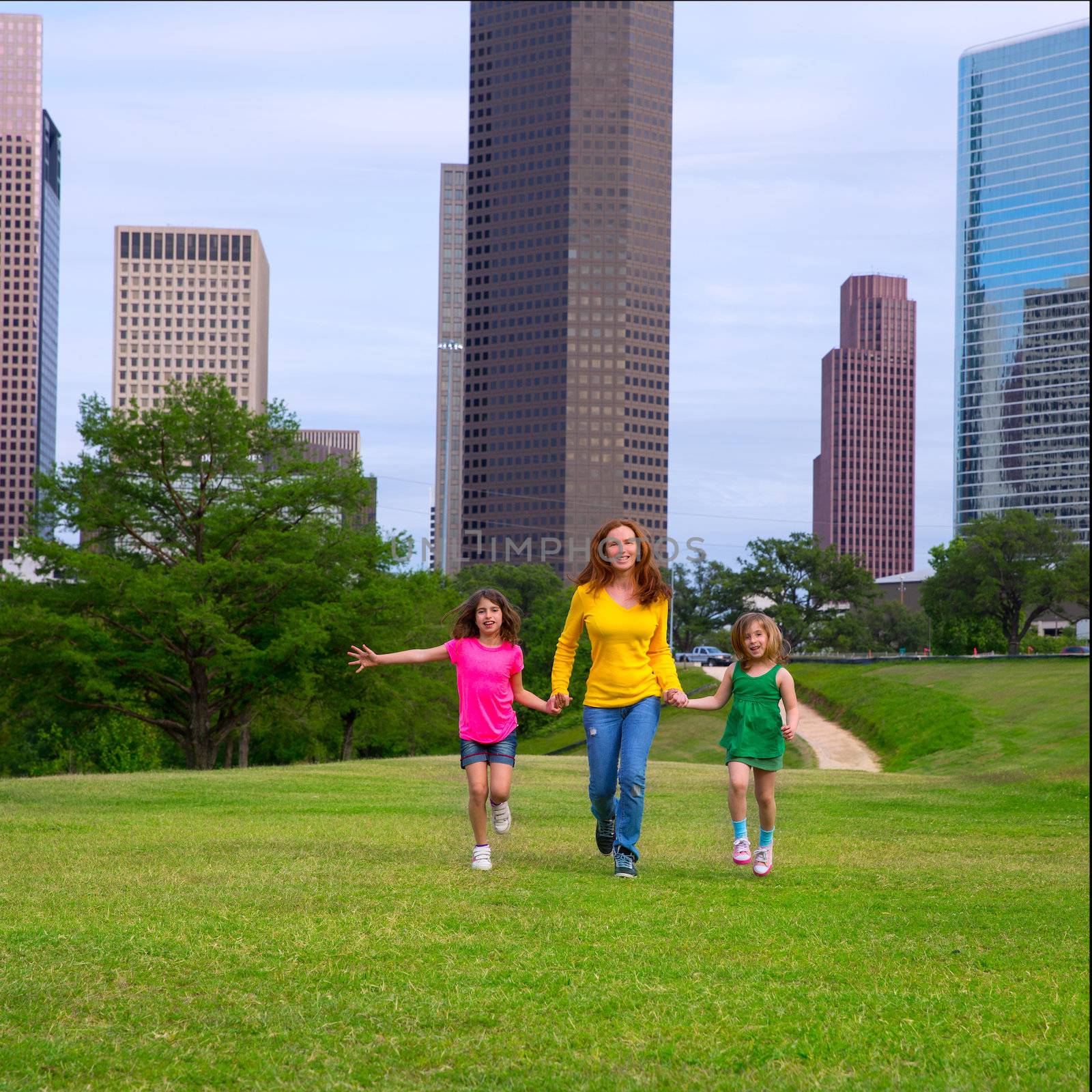 Mother and daughters walking holding hands on modern city skyline over park green lawn