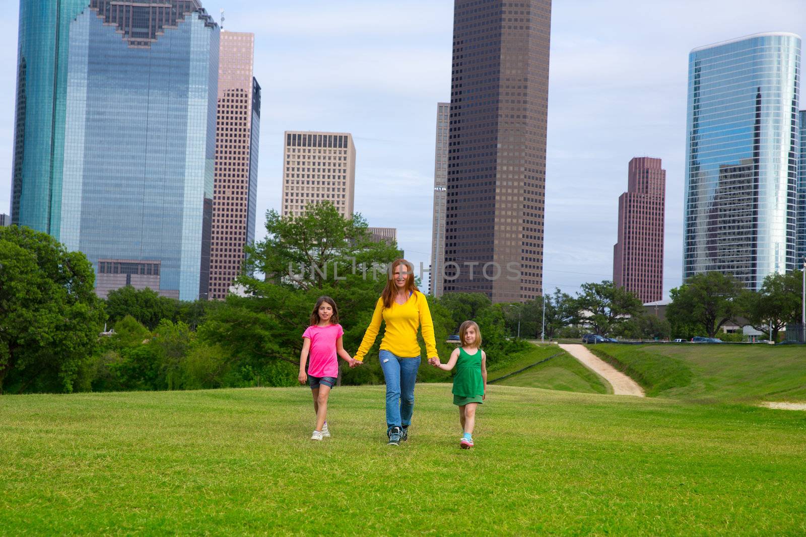 Mother and daughters walking holding hands on city skyline by lunamarina