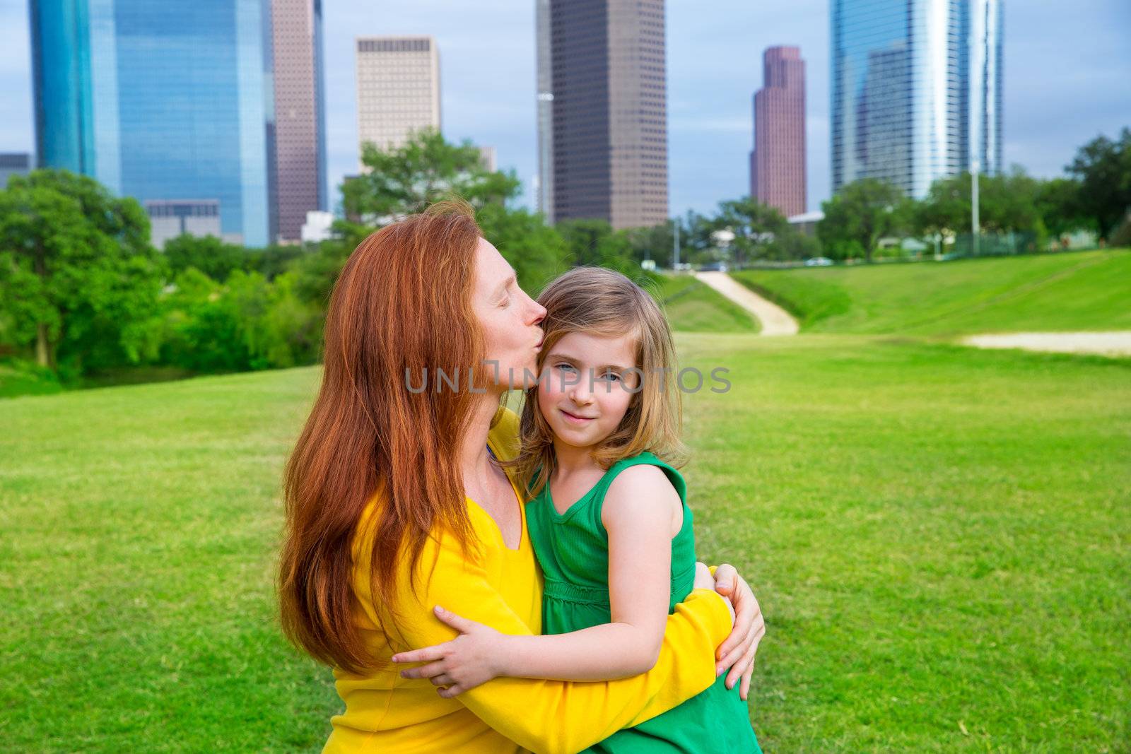 Mother and daughter happy hug kissing in park at city modern skyline background