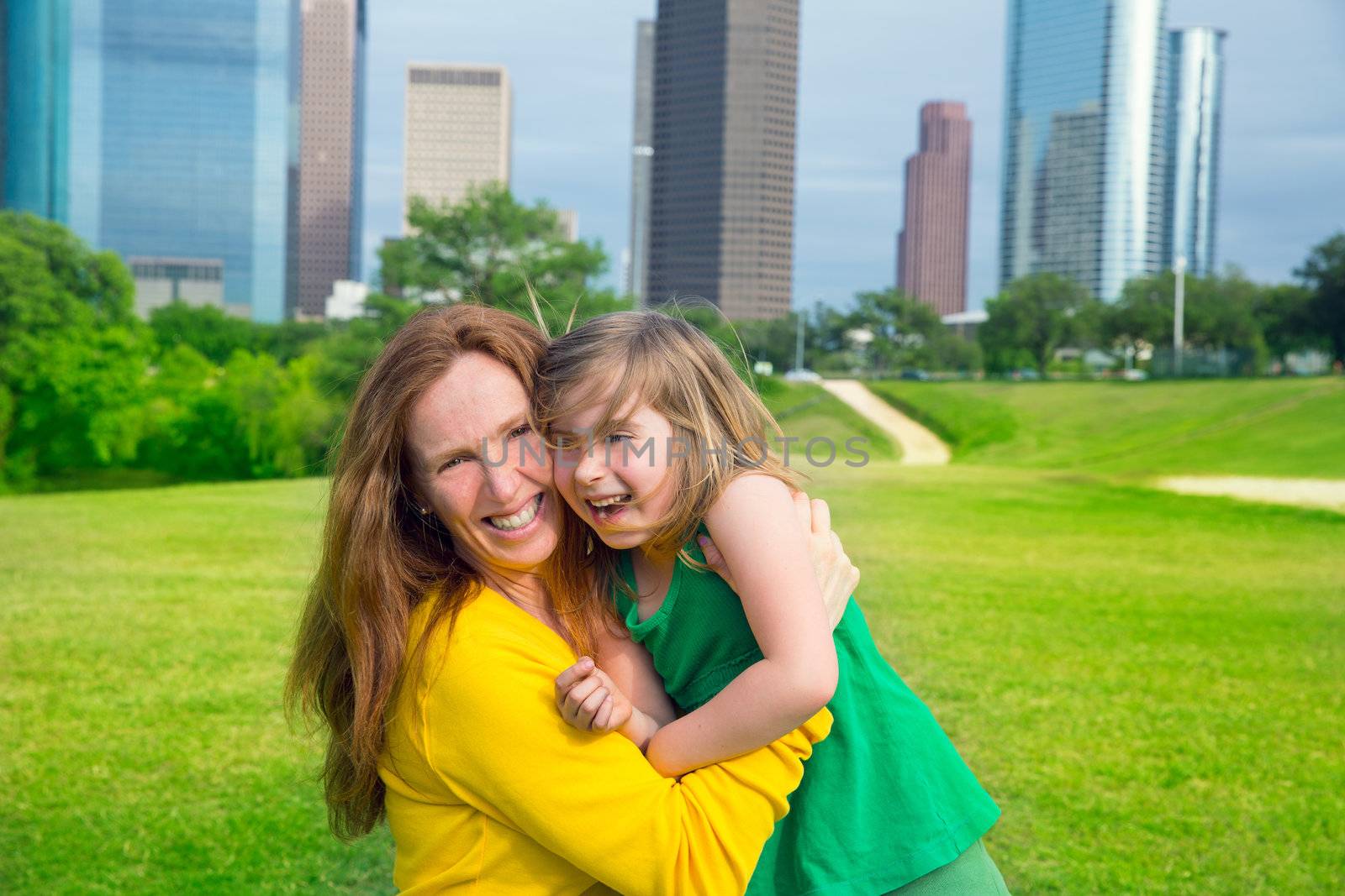 Mother and daughter happy hug laughing in park at city skyline by lunamarina