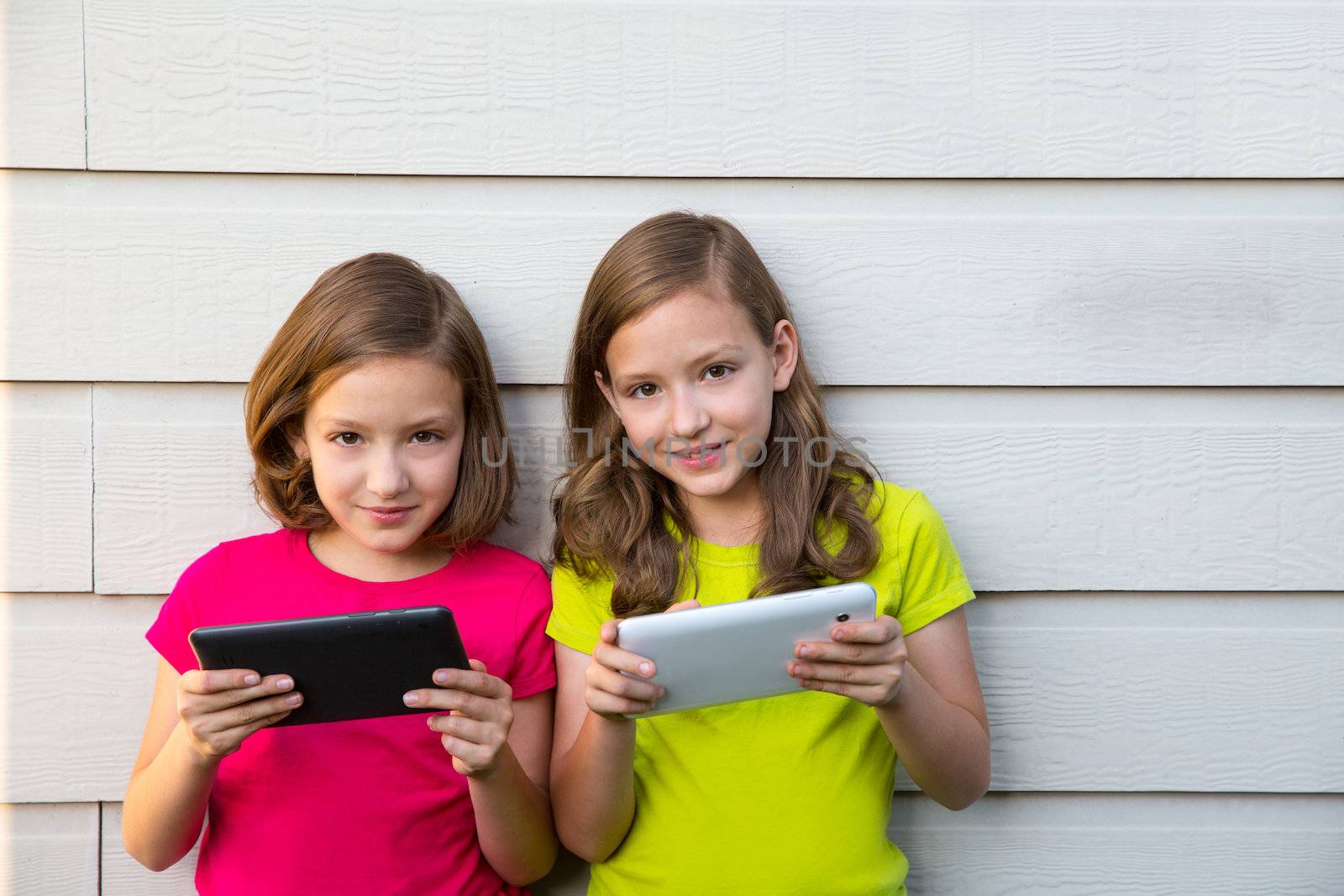 Twin sister girls playing with tablet pc happy on white wall by lunamarina