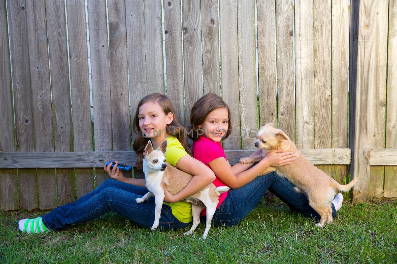 Twin sister girls playing with smartphone and chihuahua dog sitting on backyard